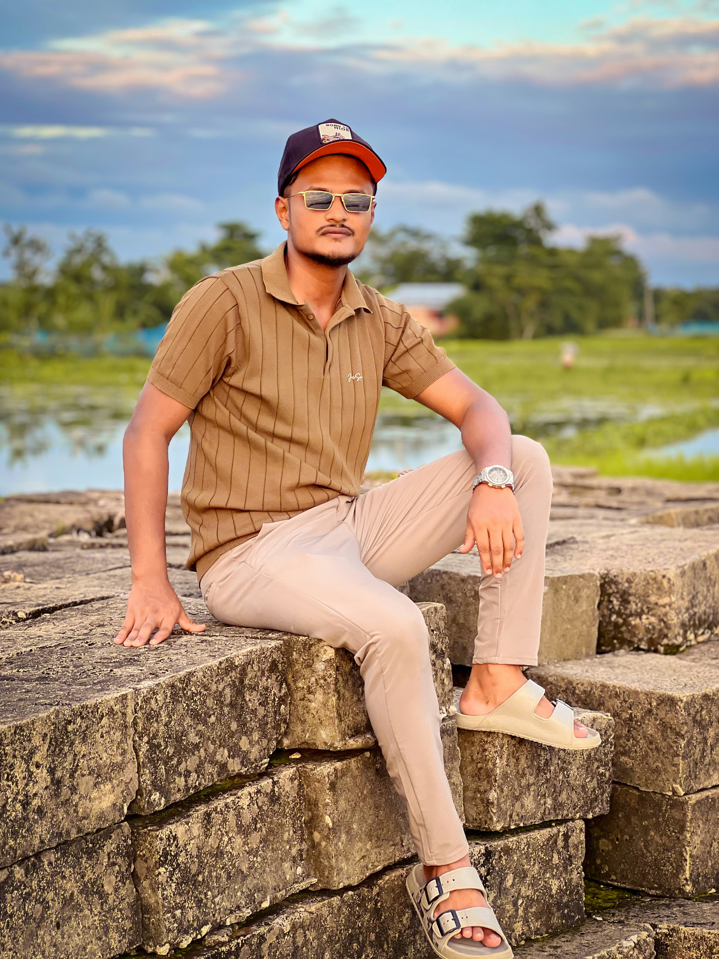 A man in a brown polo shirt and beige trousers sitting on stone blocks