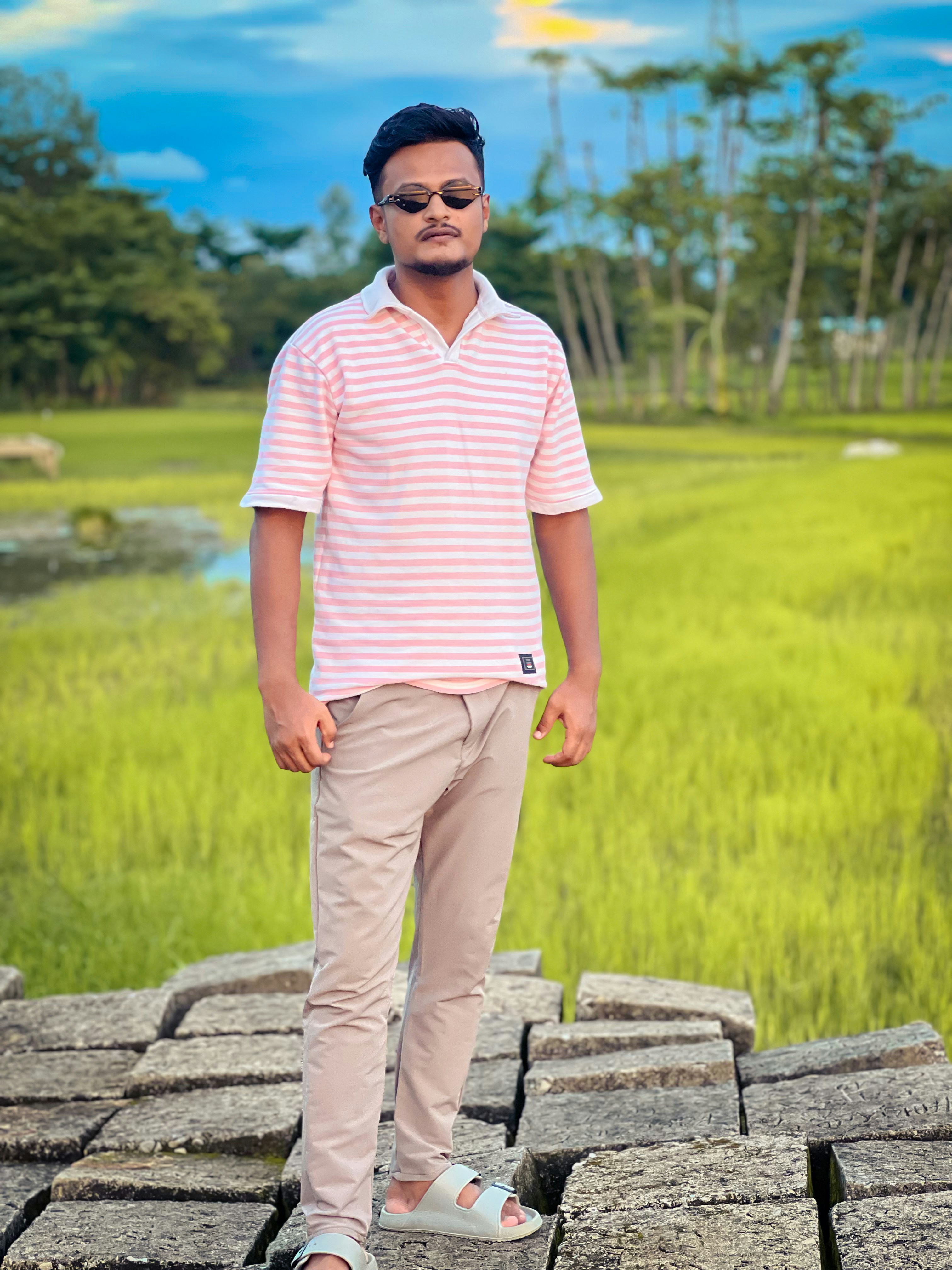 A man in a pink striped polo shirt and beige trousers on stone blocks