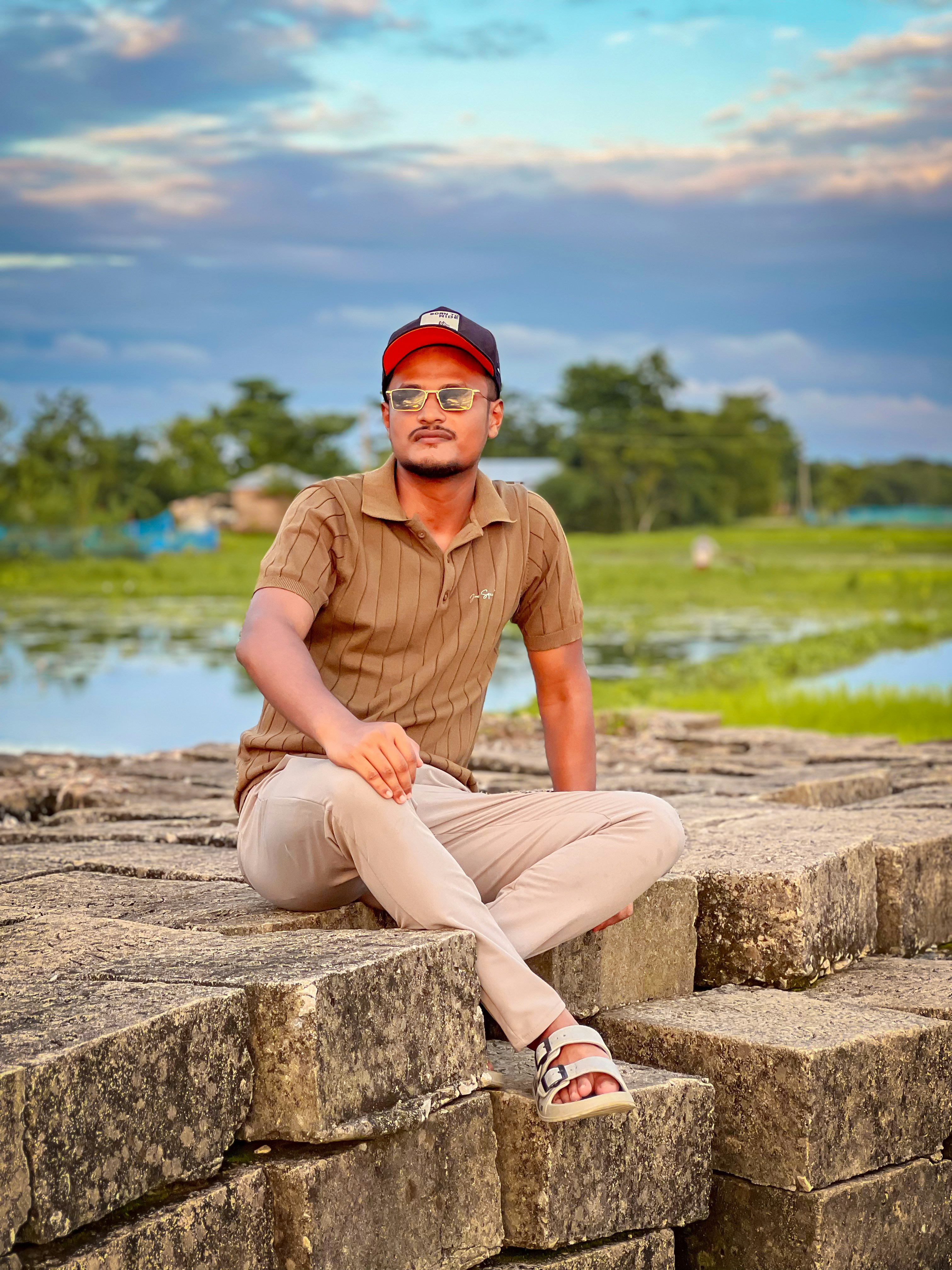 A man in a brown polo shirt and cap sitting on stone blocks