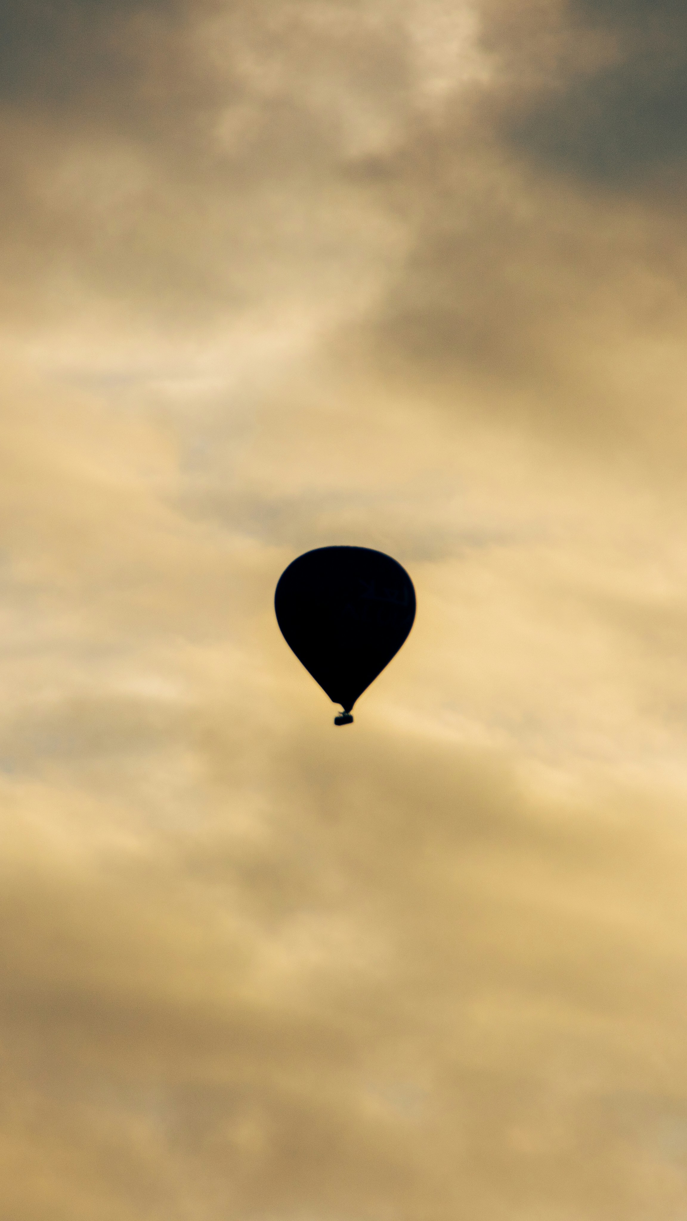 A hot air balloon in silhouette against a cloudy golden sky
