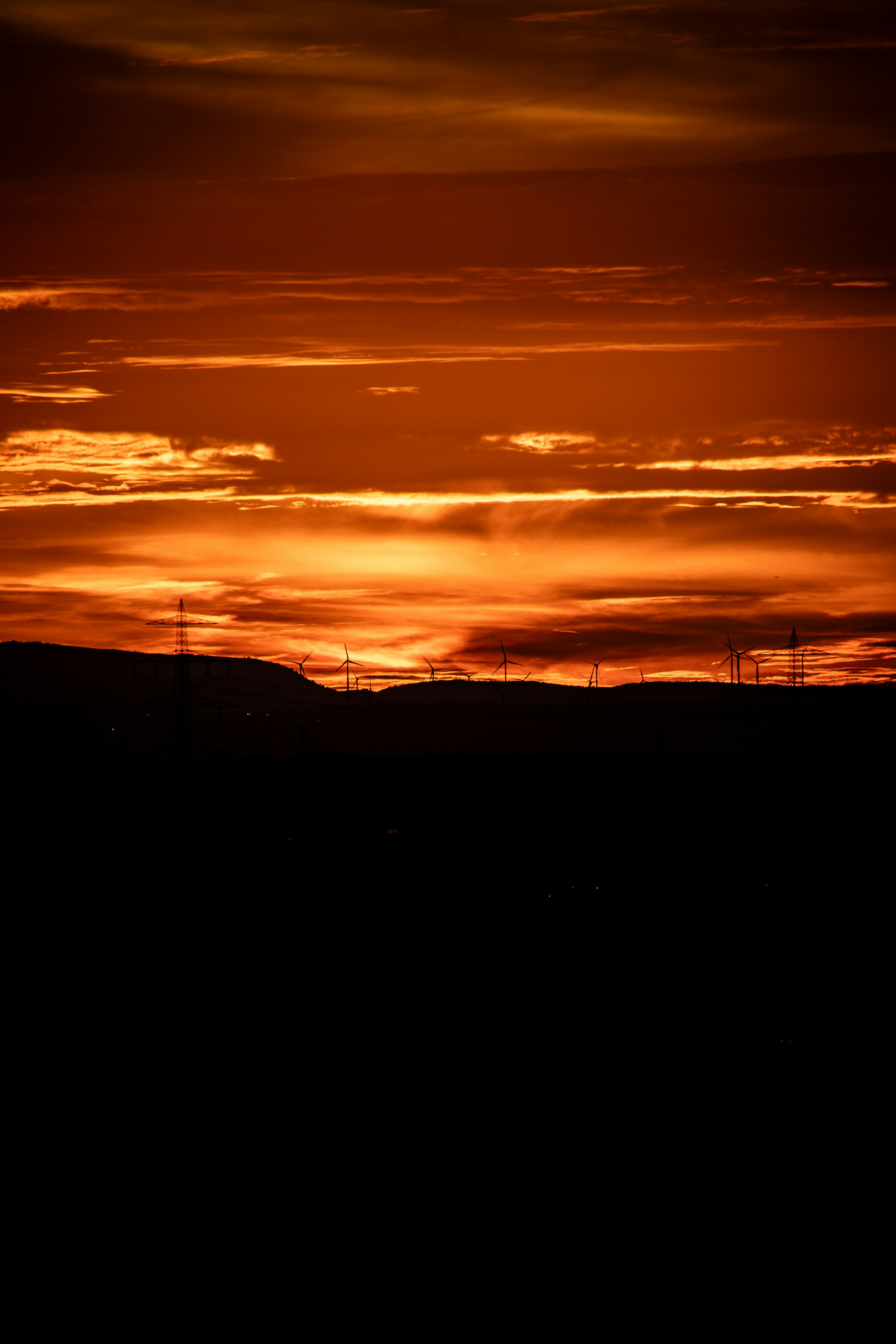Wind turbines and power pylons in silhouette against a vibrant orange sky