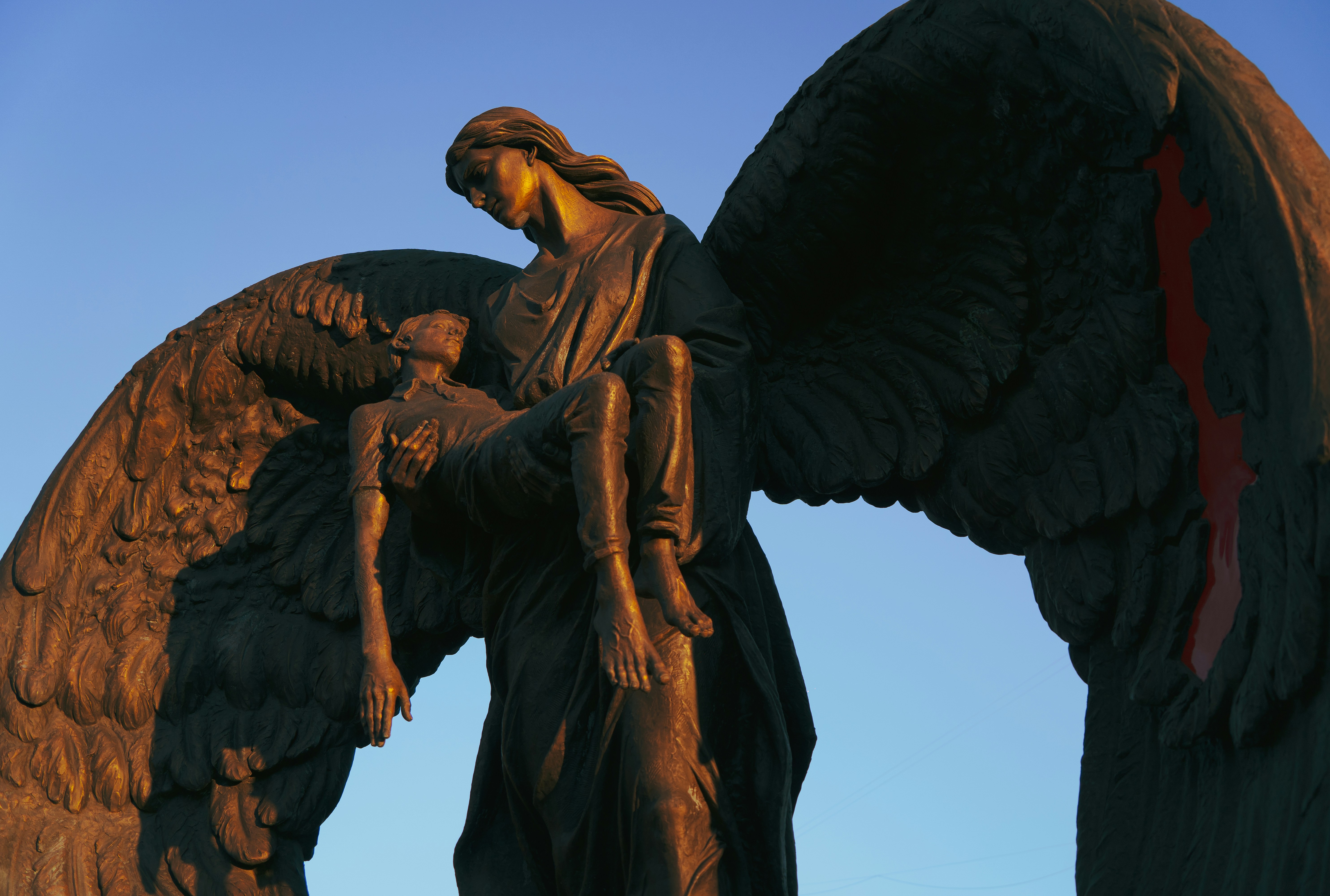 A bronze statue of an angel holding a child against a clear blue sky