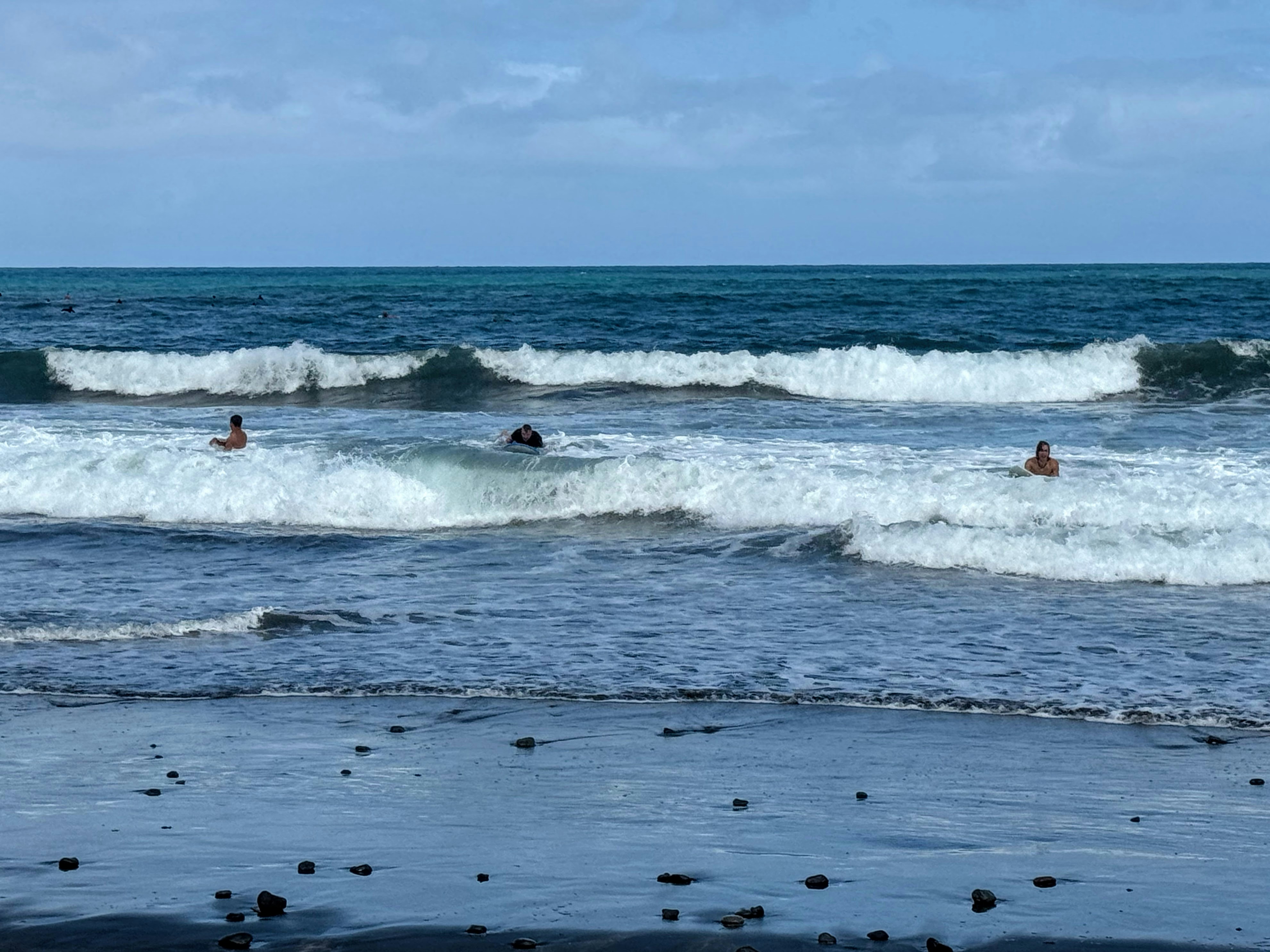Three people surfing in the ocean waves under a blue sky