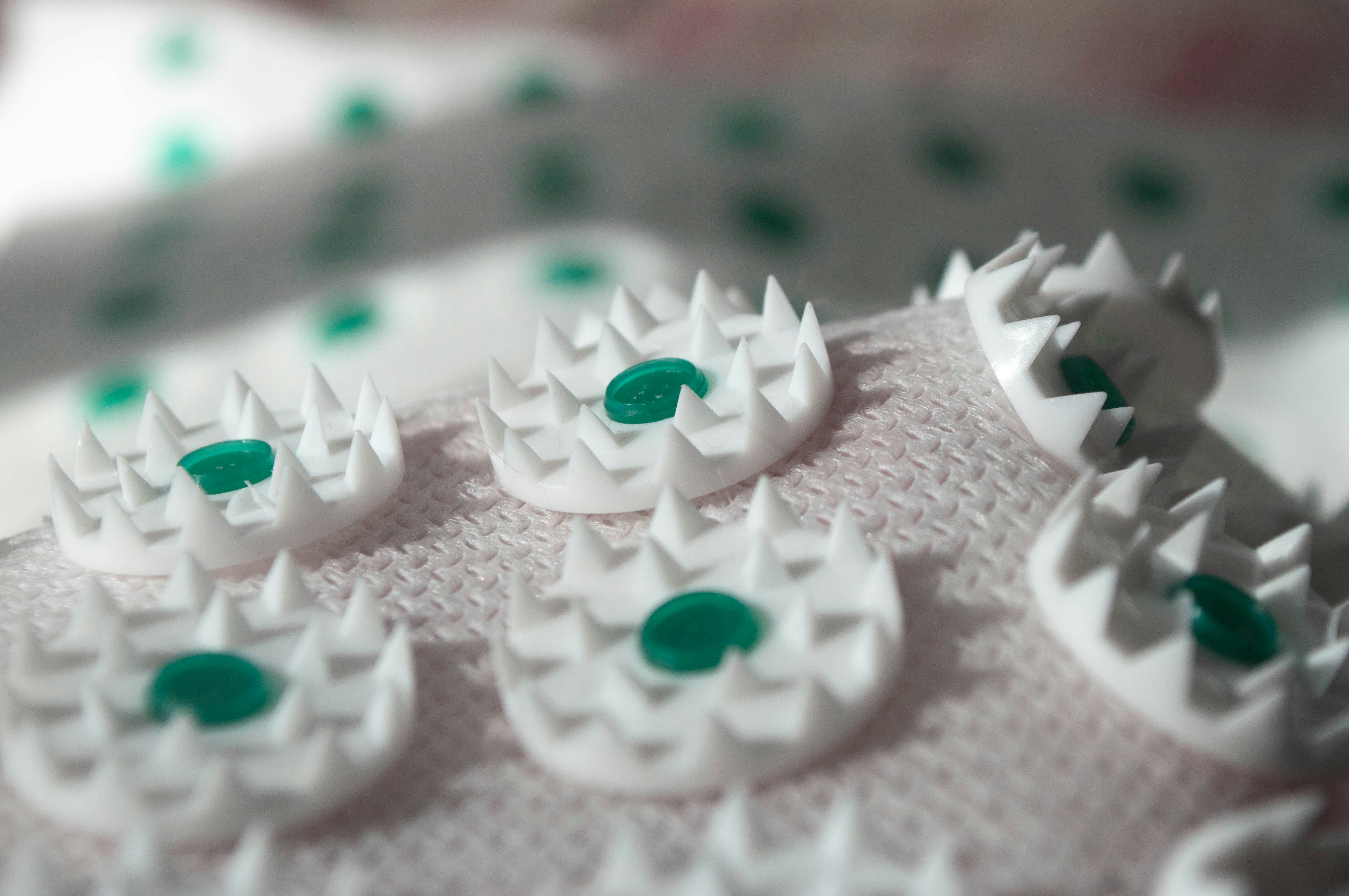 White plastic discs with sharp spikes and green centers on a textured fabric