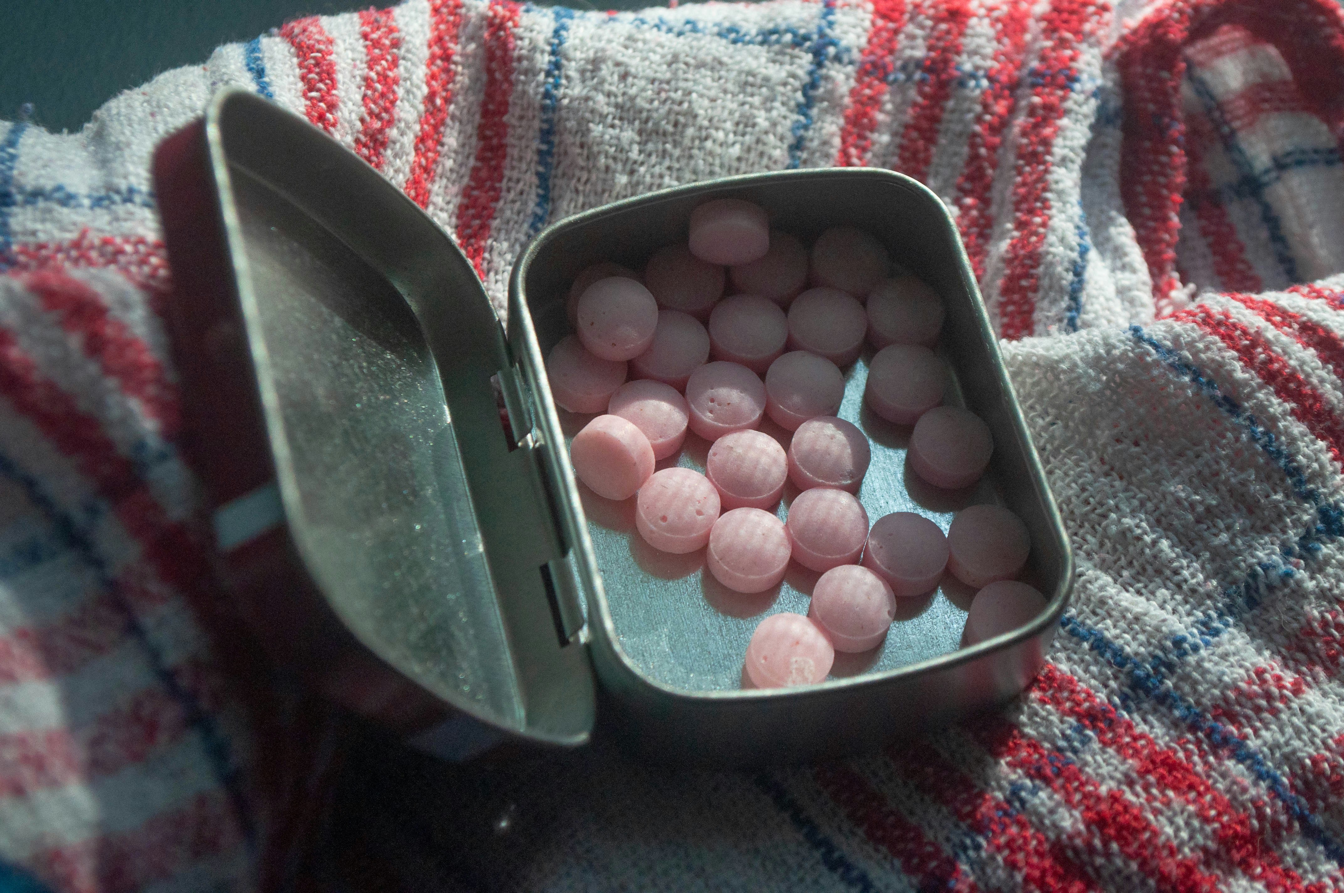 Small pink round candies inside an open metal tin on a striped cloth