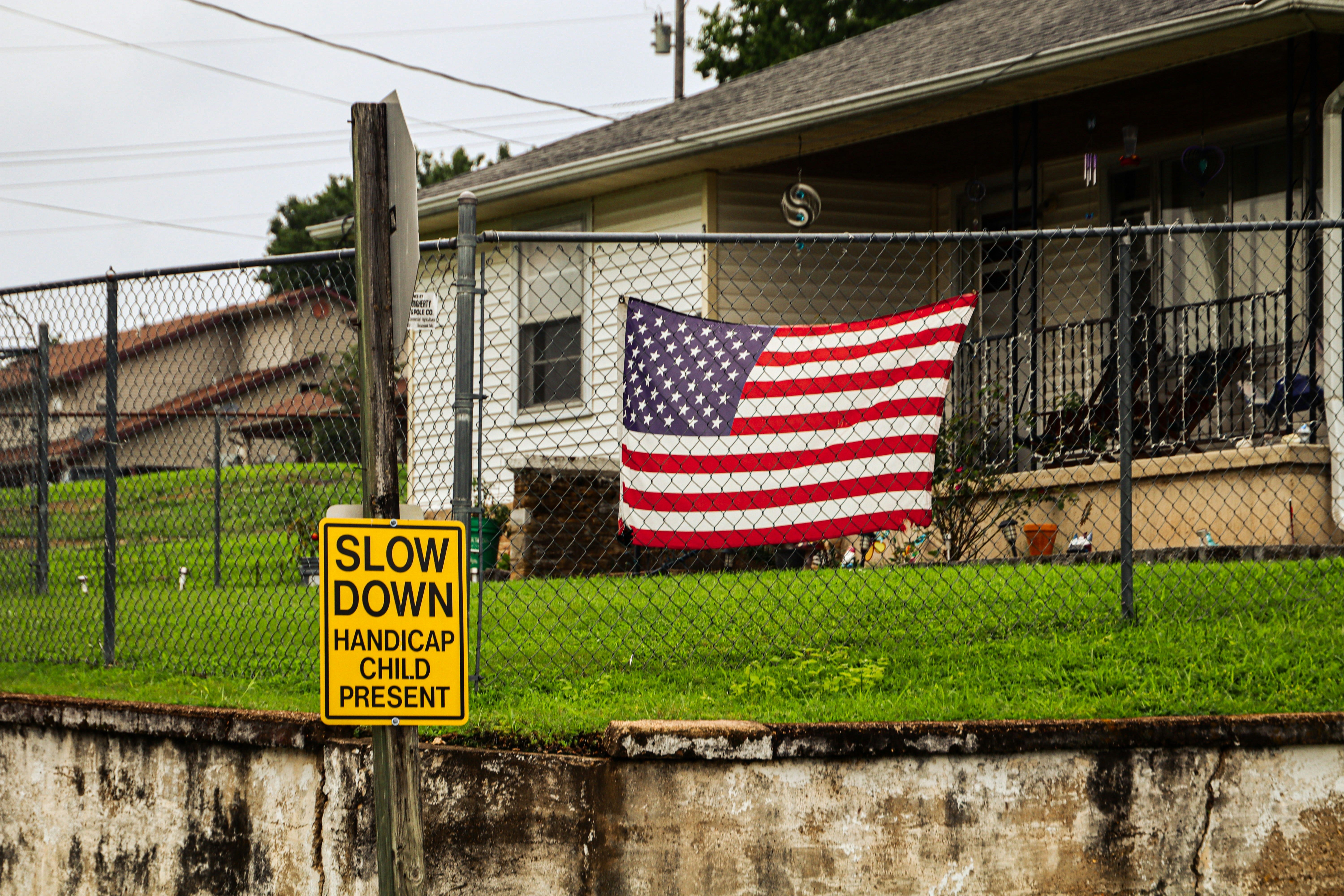 An American flag hanging on a chain link fence near a yellow warning sign