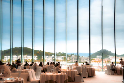 Guests at round tables in a dining room with tall windows