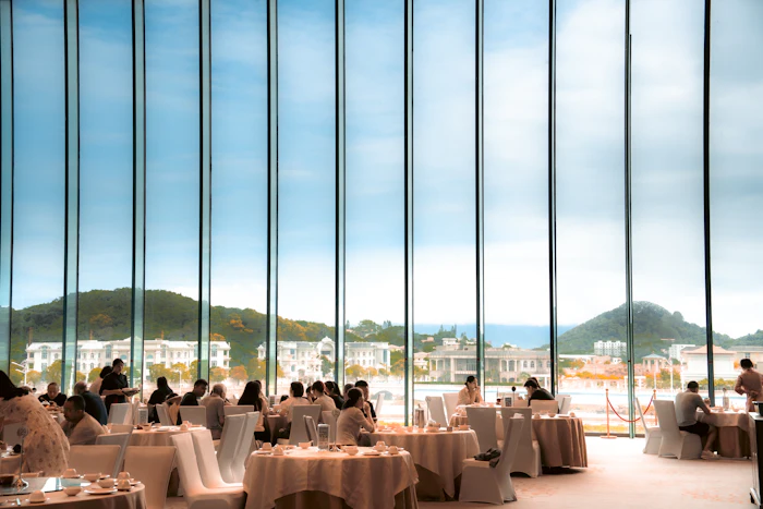 Guests at round tables in a dining room with tall windows