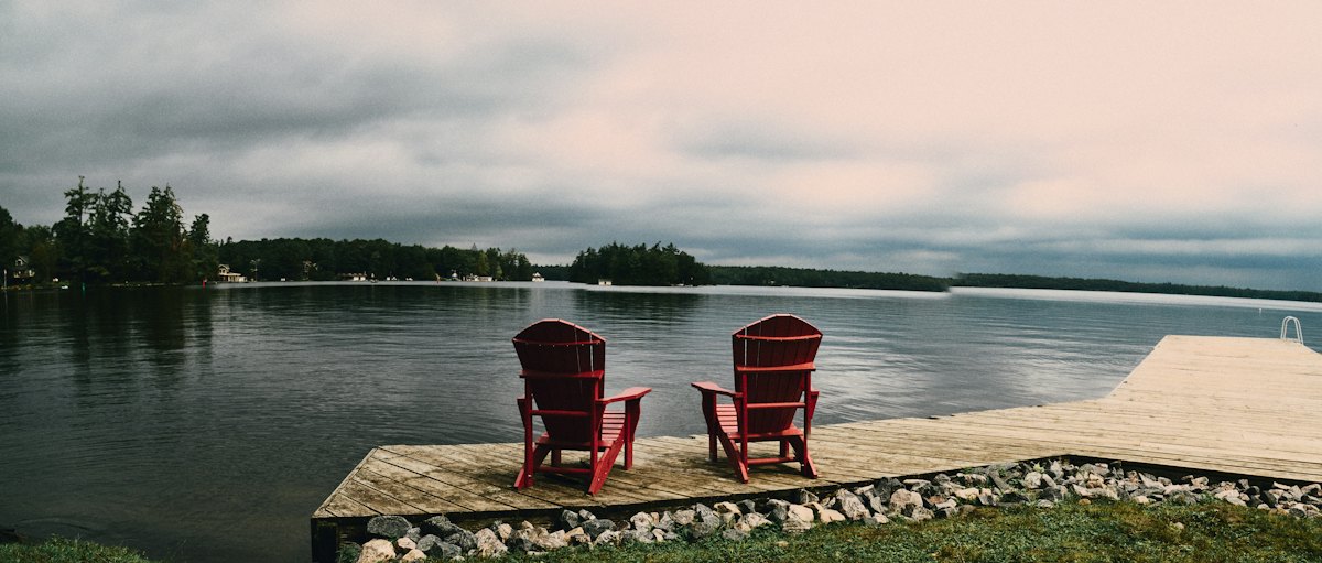 Two red Adirondack chairs on a lakeside dock