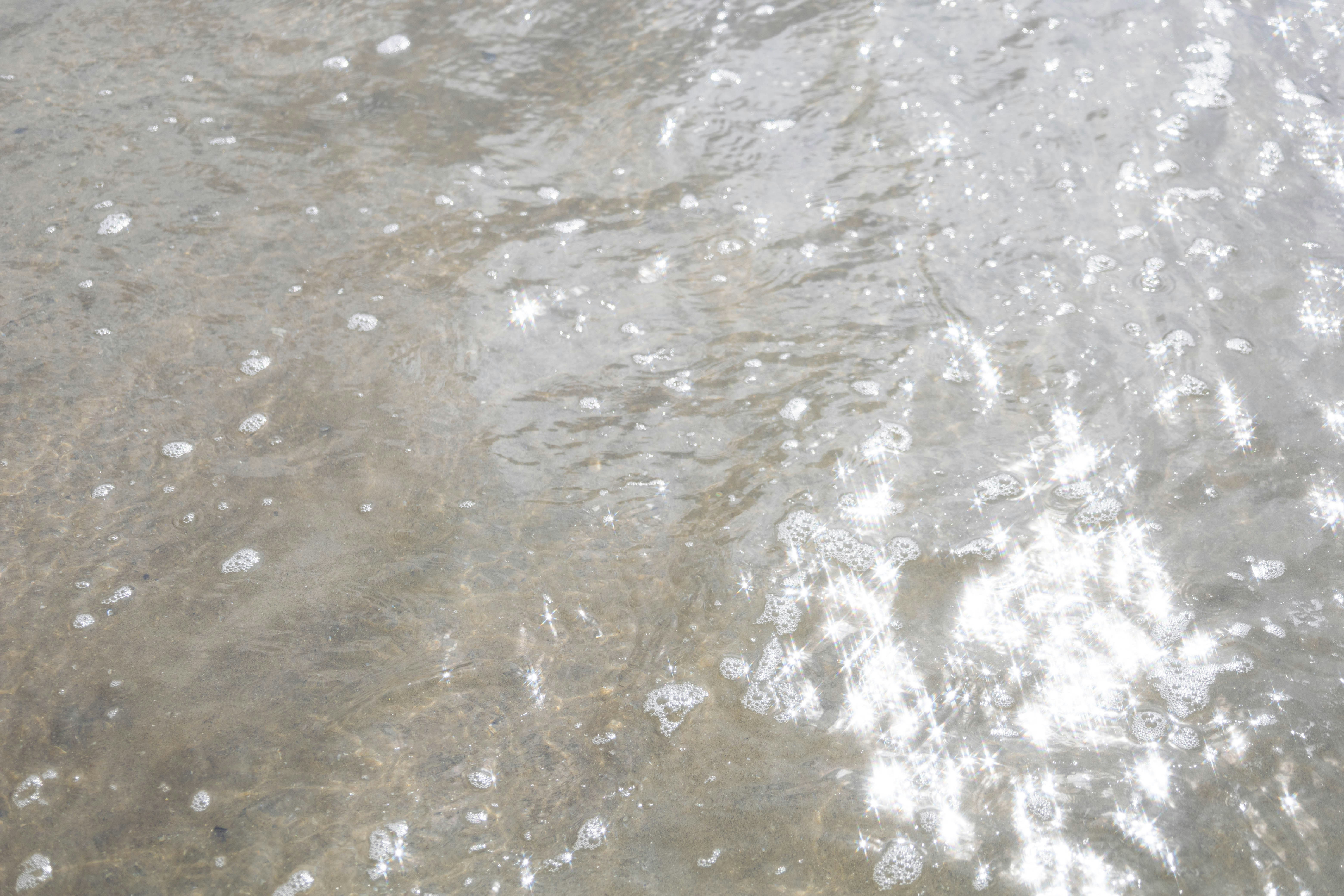 Sunlight reflecting off shallow rippling water with small white foam bubbles
