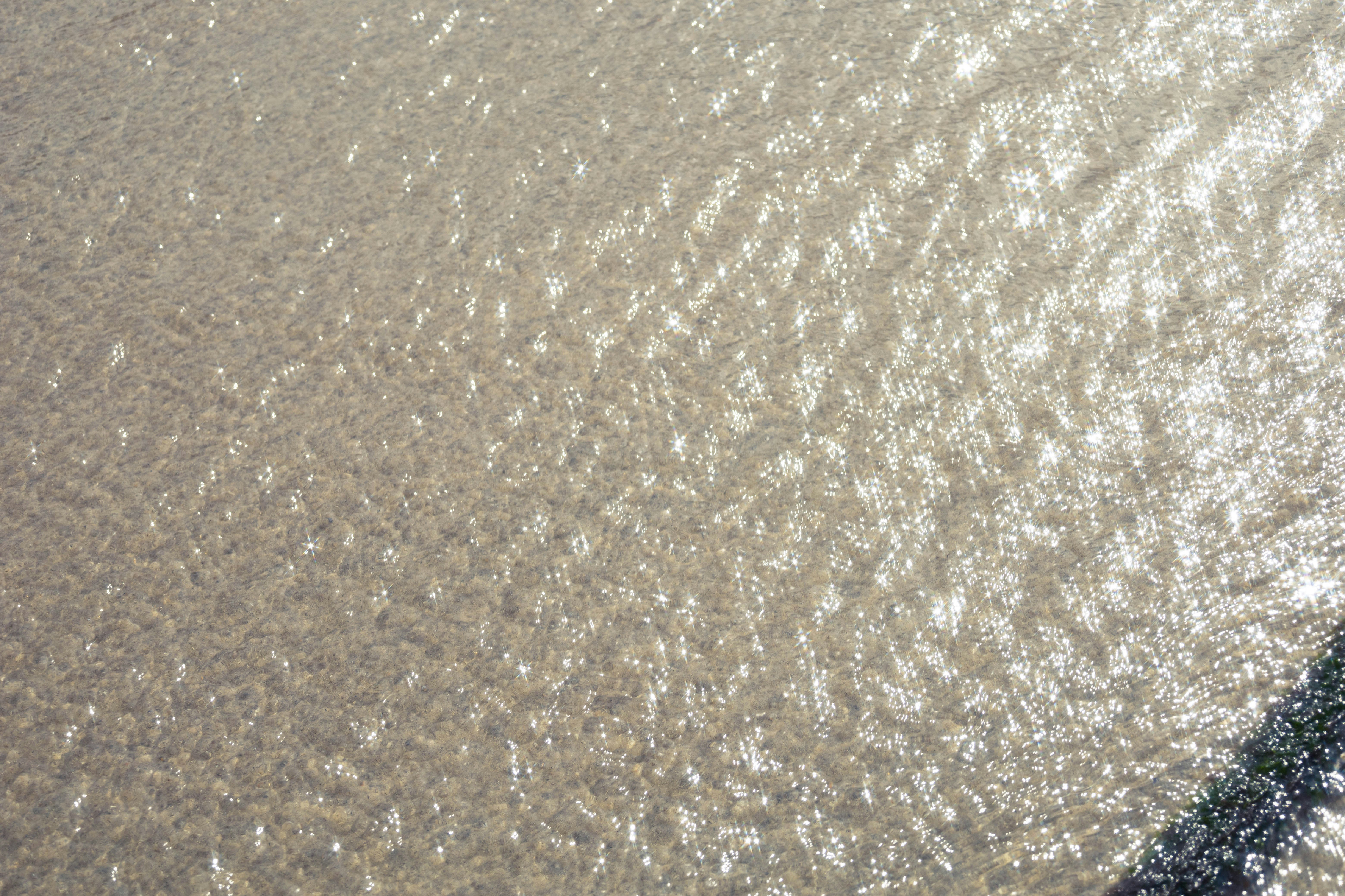 Sunlight reflecting off the rippling surface of shallow water over a sandy bottom
