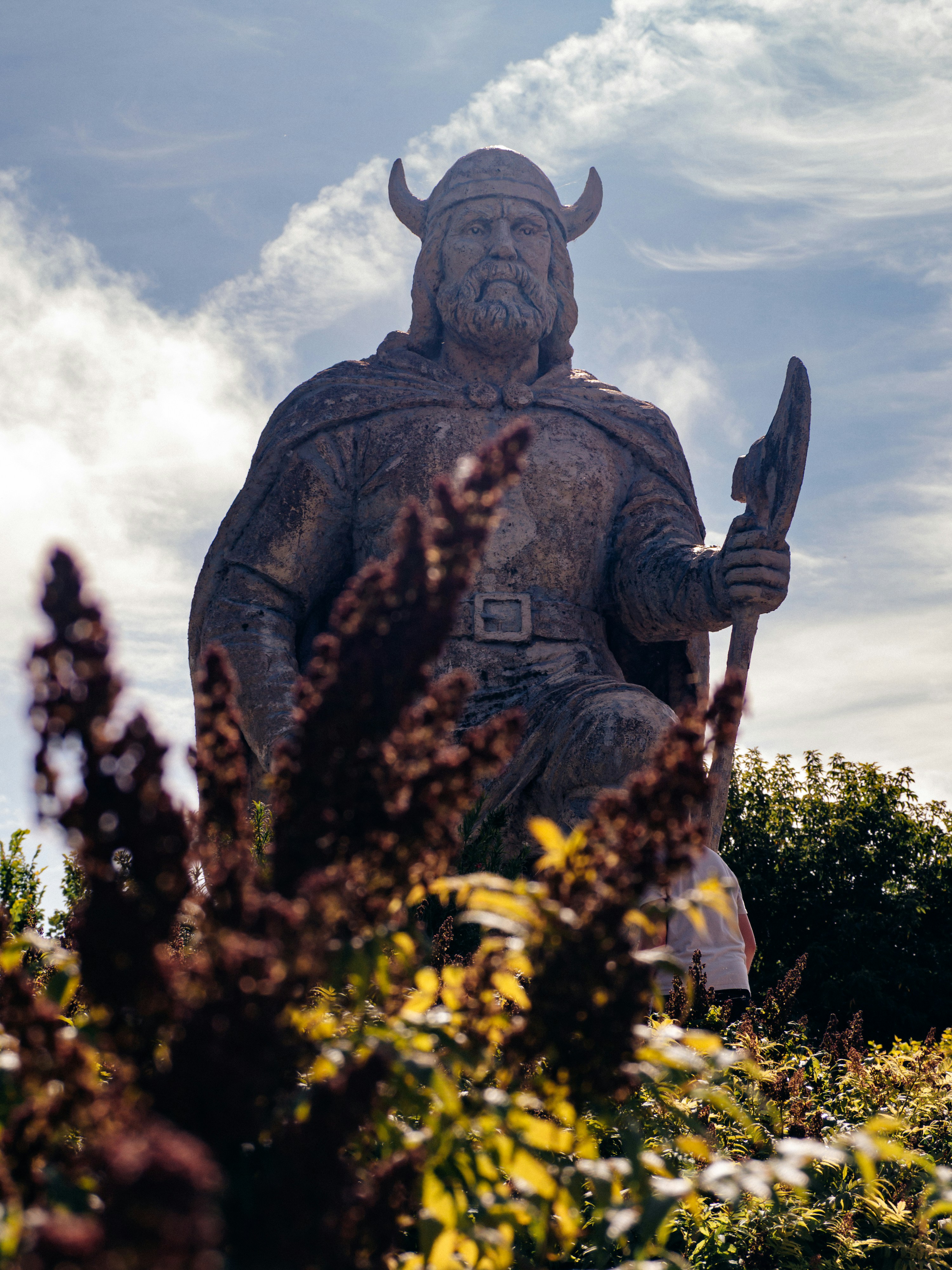 A large stone statue of a Viking warrior holding a spear in a garden