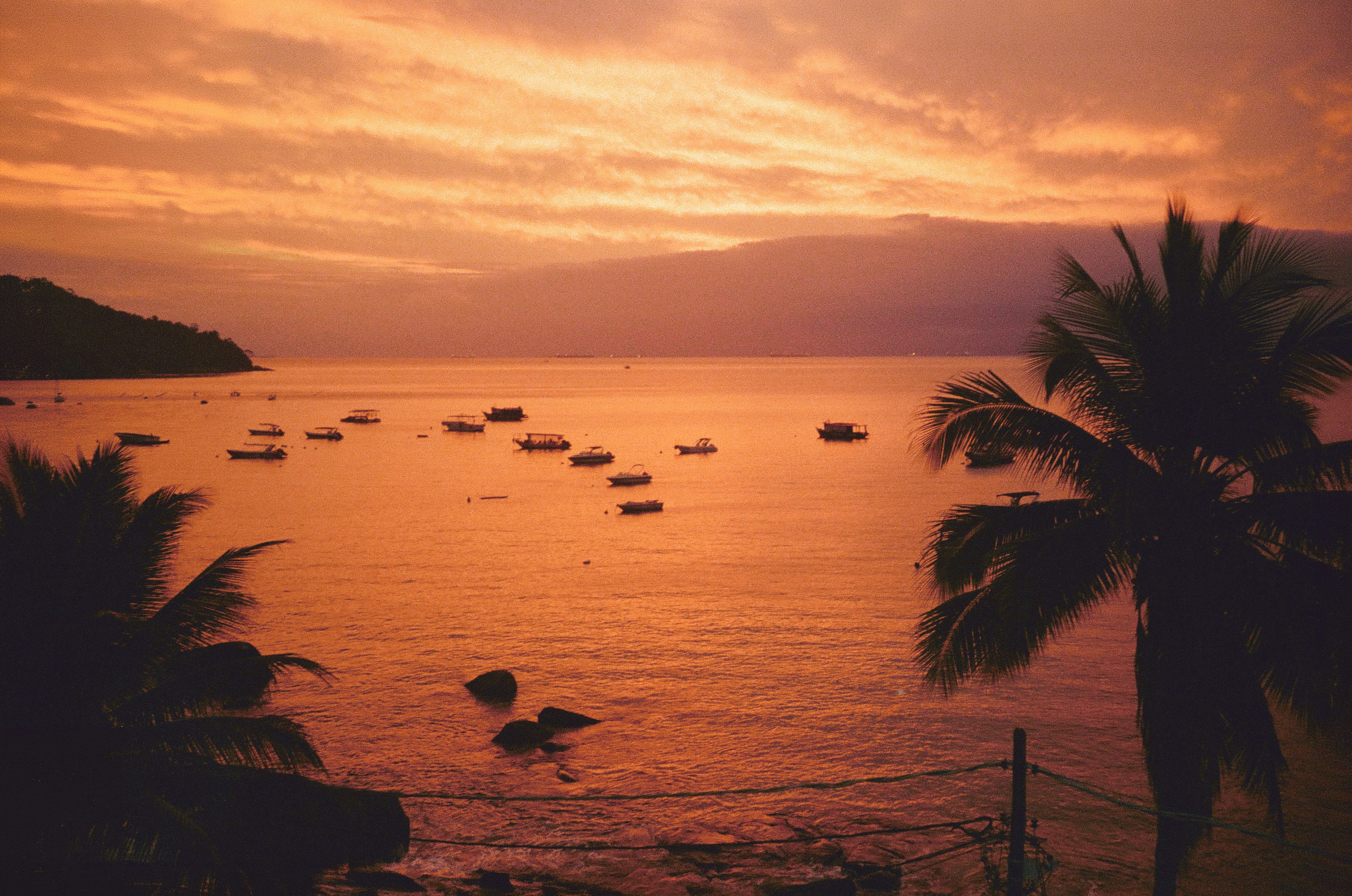 Kleine Boote, die in einer ruhigen Bucht unter einem warmen orangefarbenen Himmel vor Anker lagen.