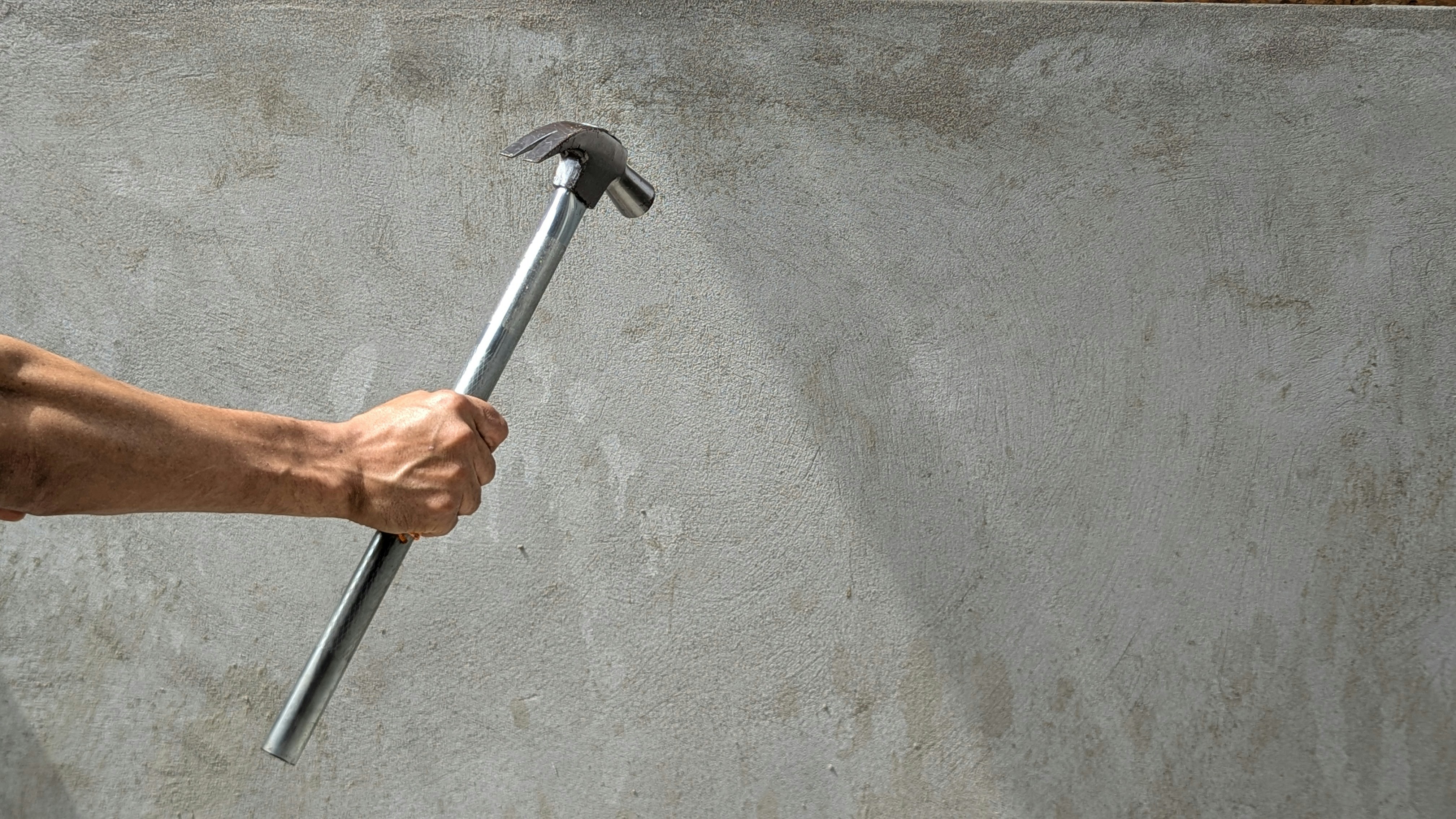 Hand holding a claw hammer against a concrete wall