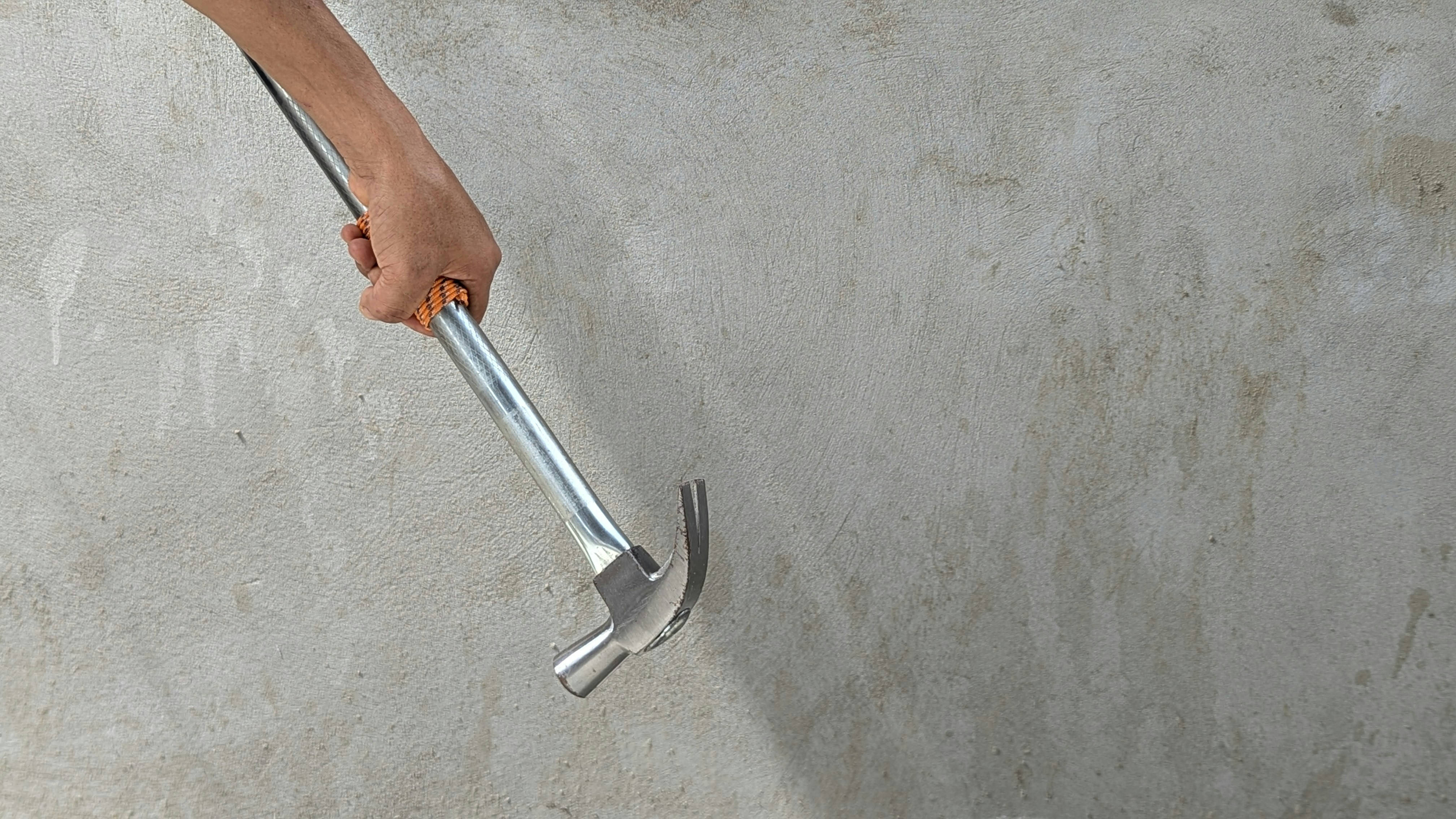A hand holding a metal hammer against a textured grey concrete wall