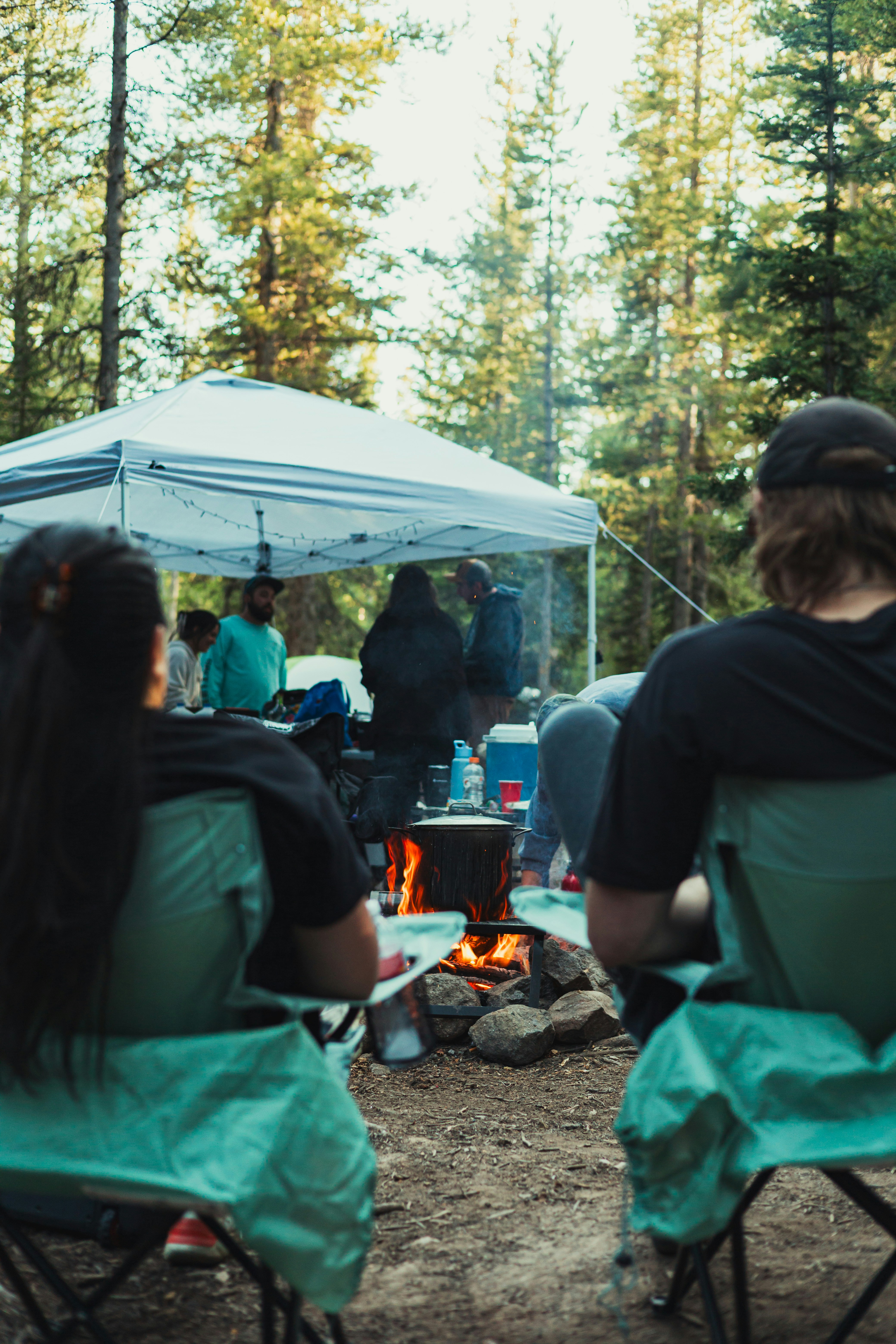 People sitting in folding chairs around a campfire under a white canopy