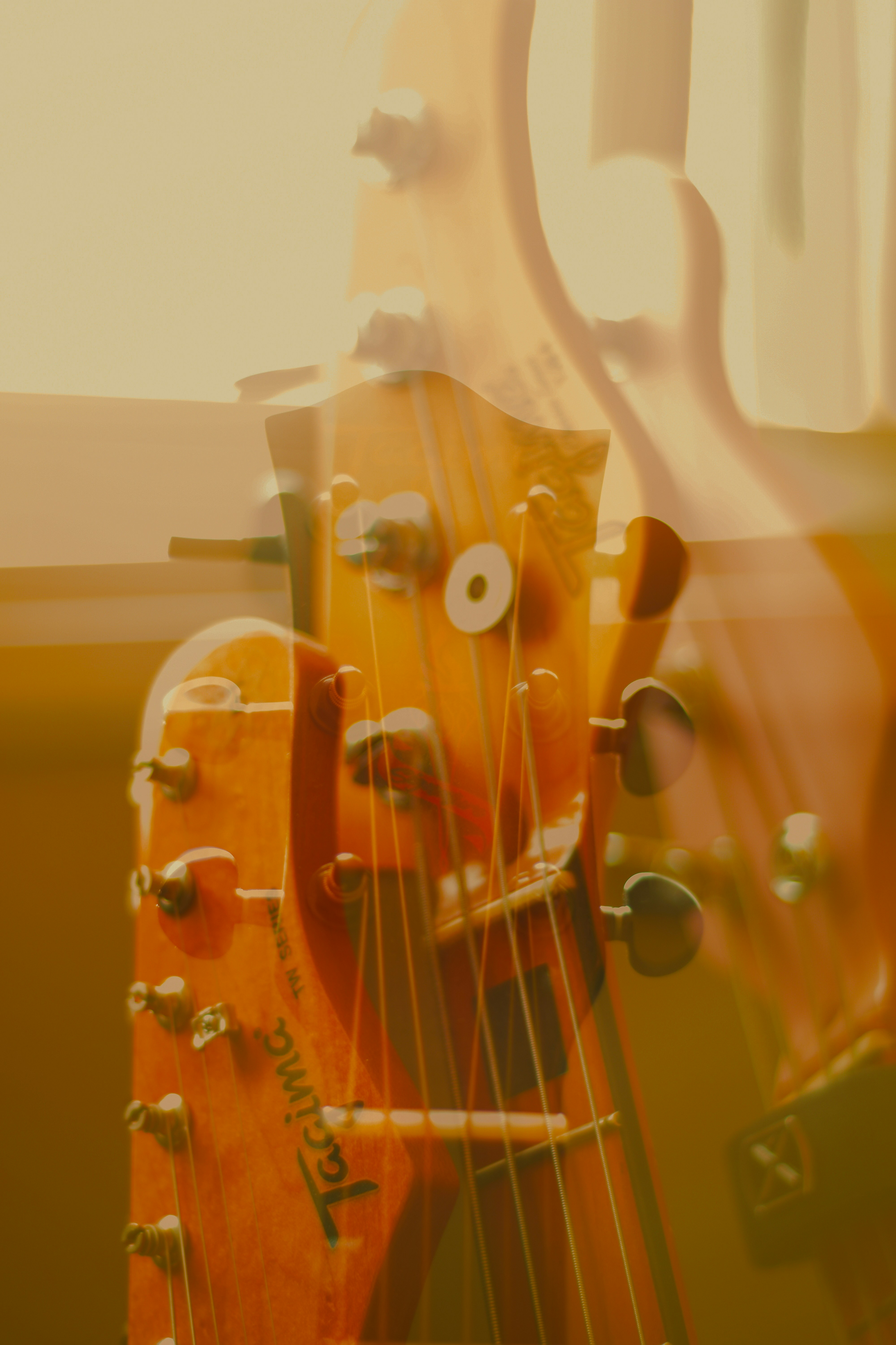 Uma dupla exposição de um headstock de guitarra de madeira em uma luz dourada e quente