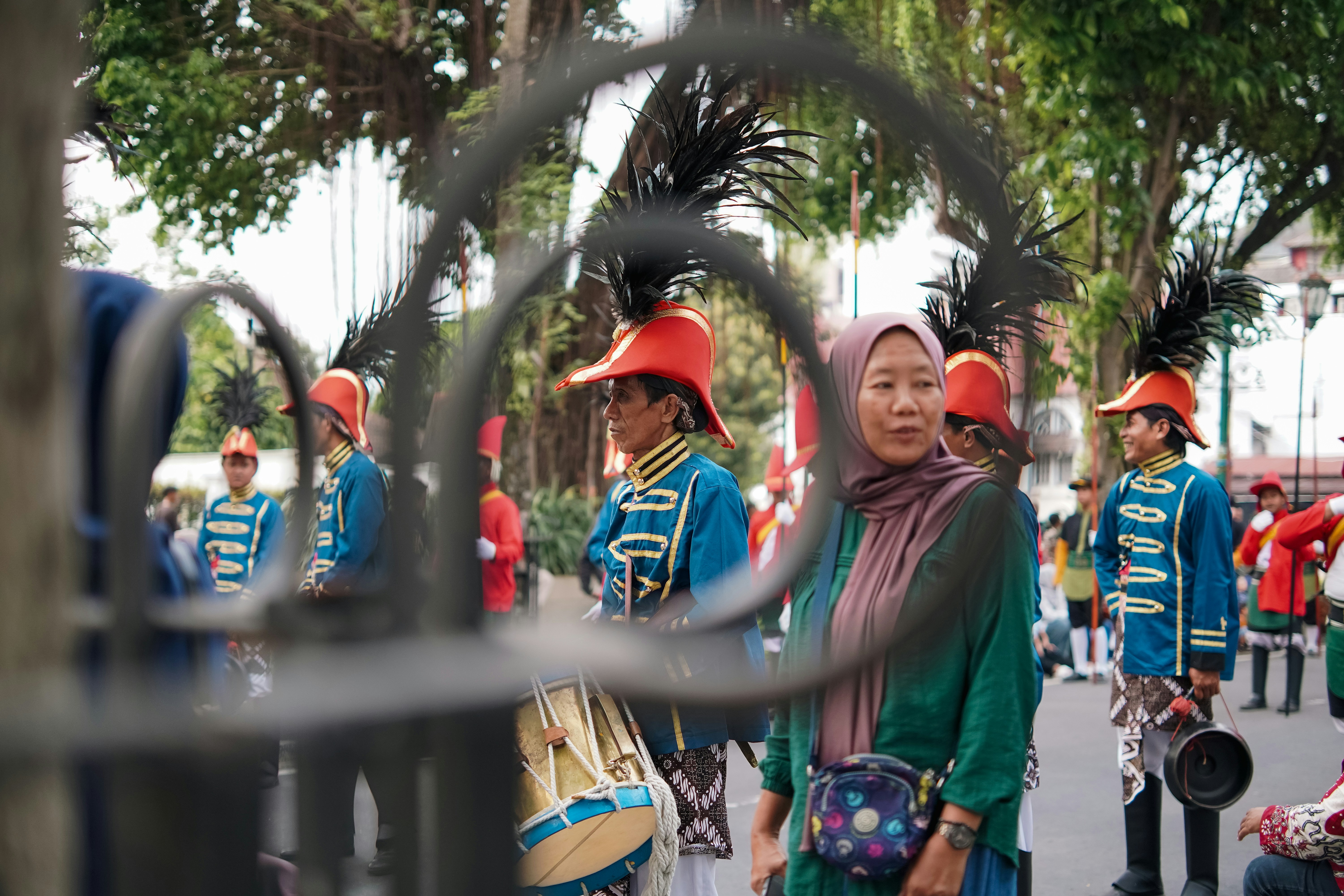 Seorang wanita mengenakan hijab menonton marching band dengan seragam biru tradisional