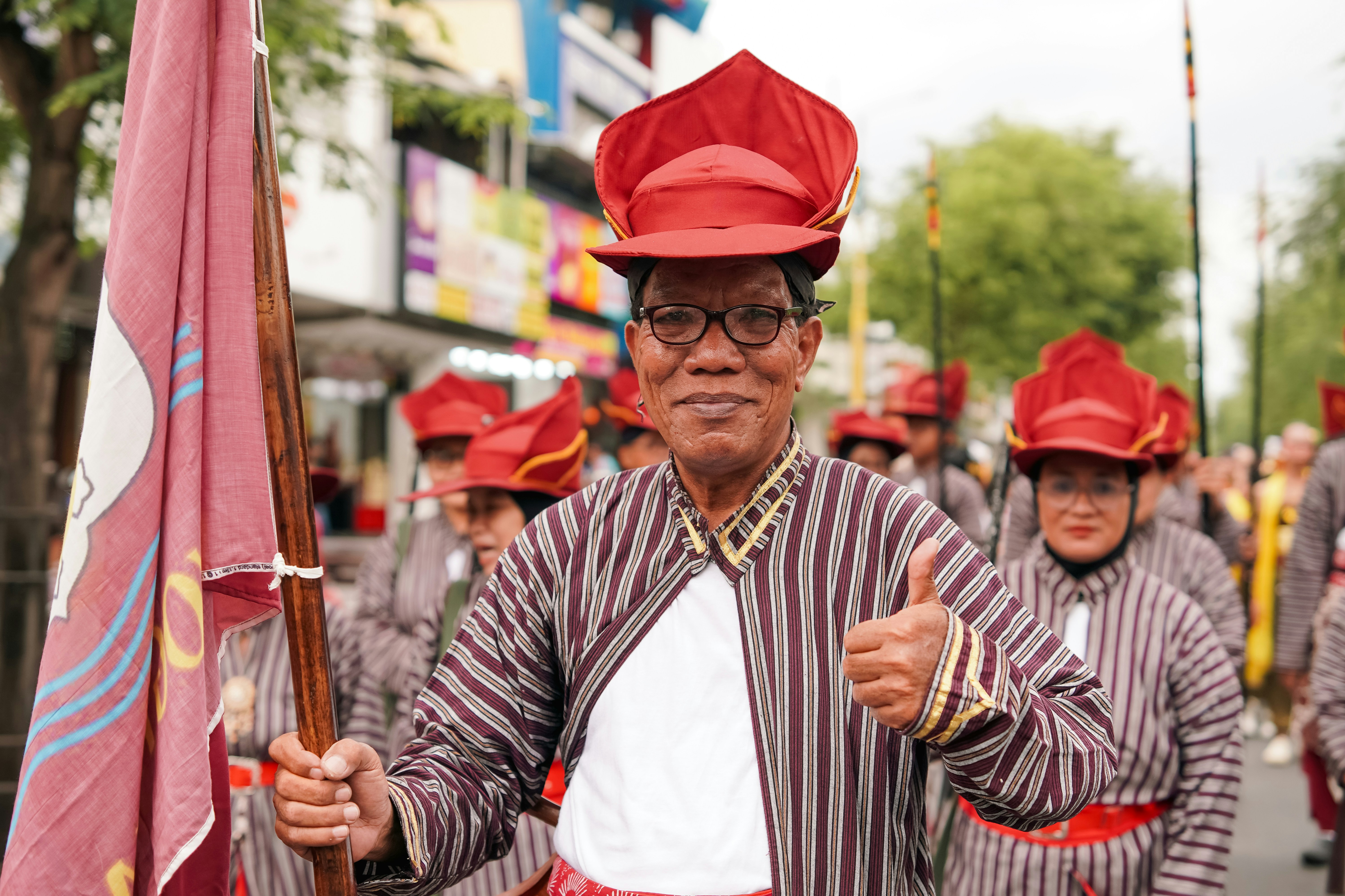 Seorang pria dengan jaket garis tradisional dan topi merah memberi jempol