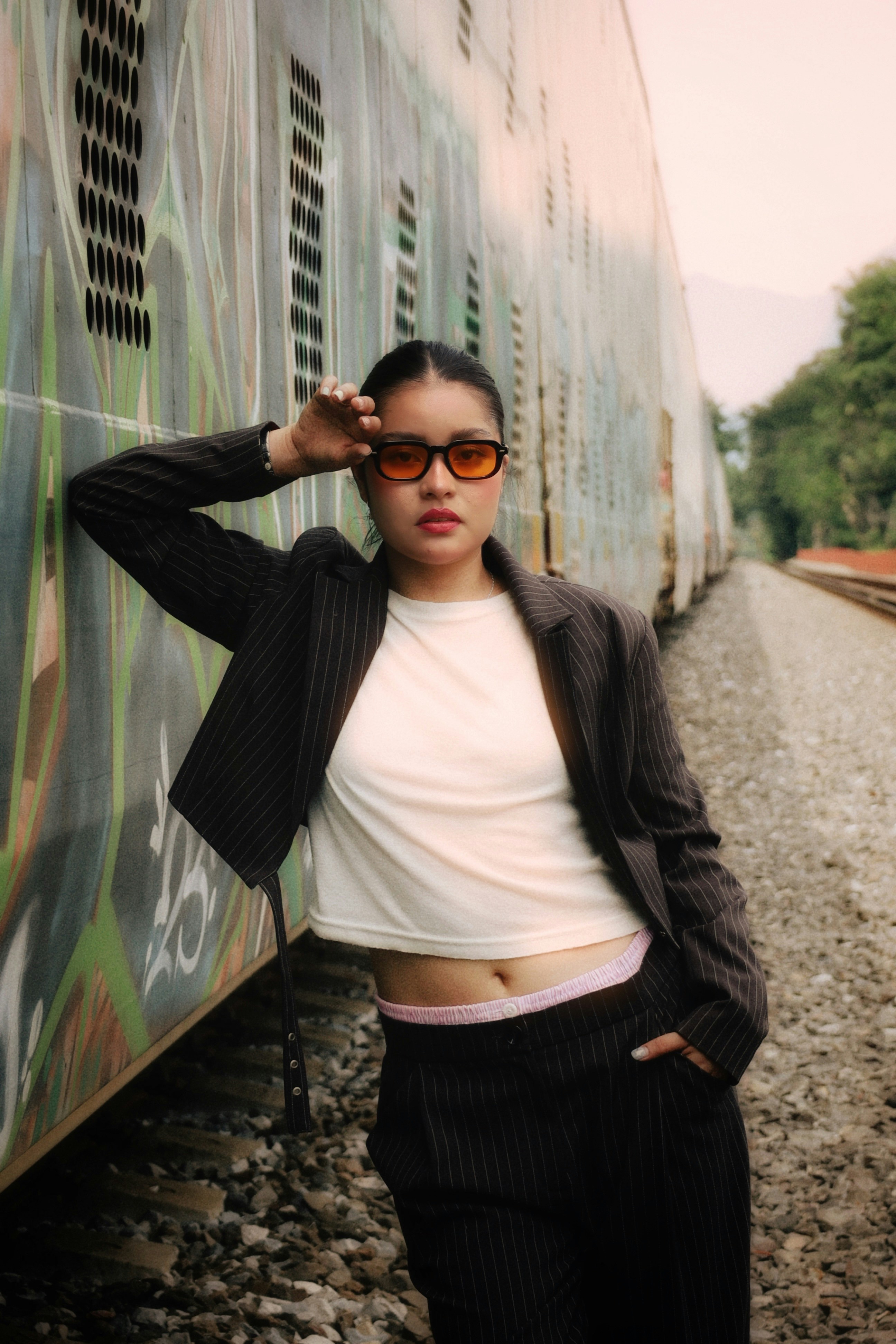 A person in a pinstripe suit and orange sunglasses leaning against a graffiti-covered train