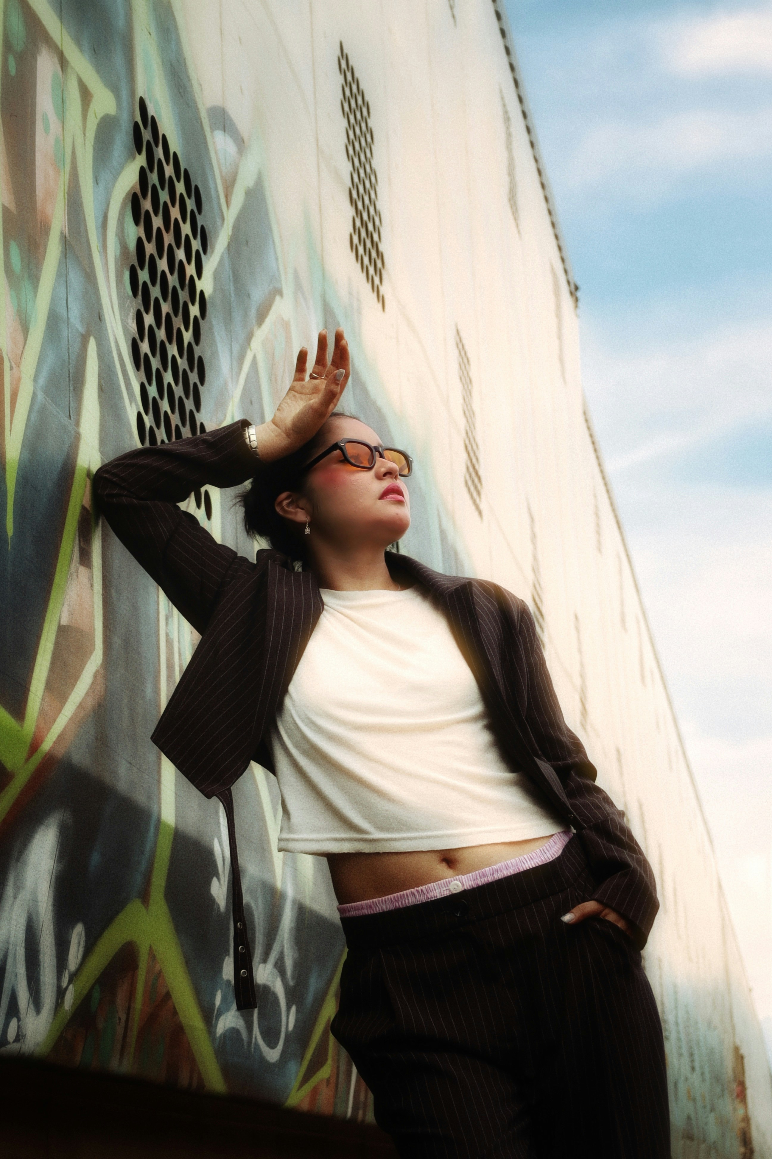 A person in a pinstripe suit leaning against a graffiti covered wall