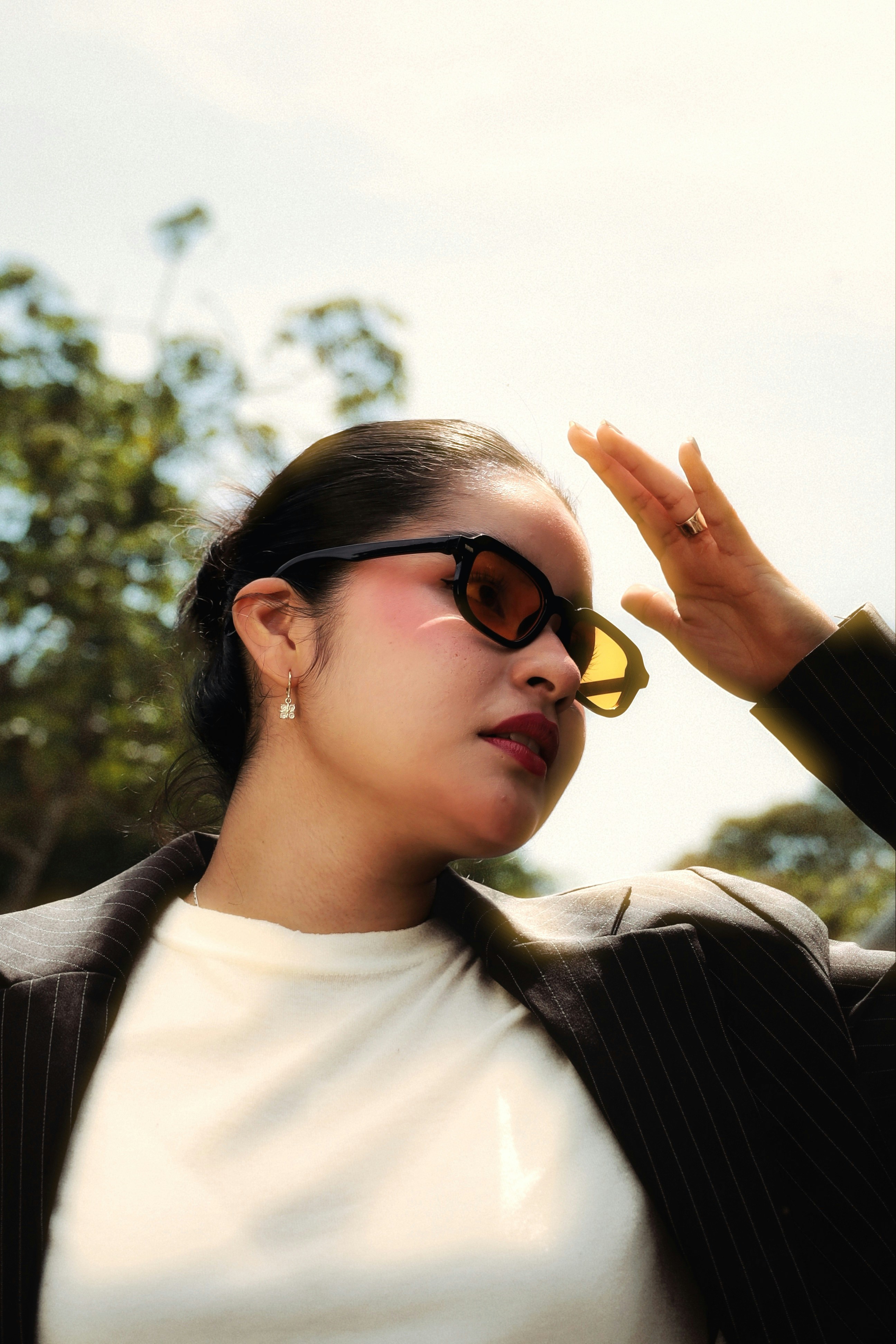 A woman in a pinstriped blazer shielding her eyes from the sun outdoors