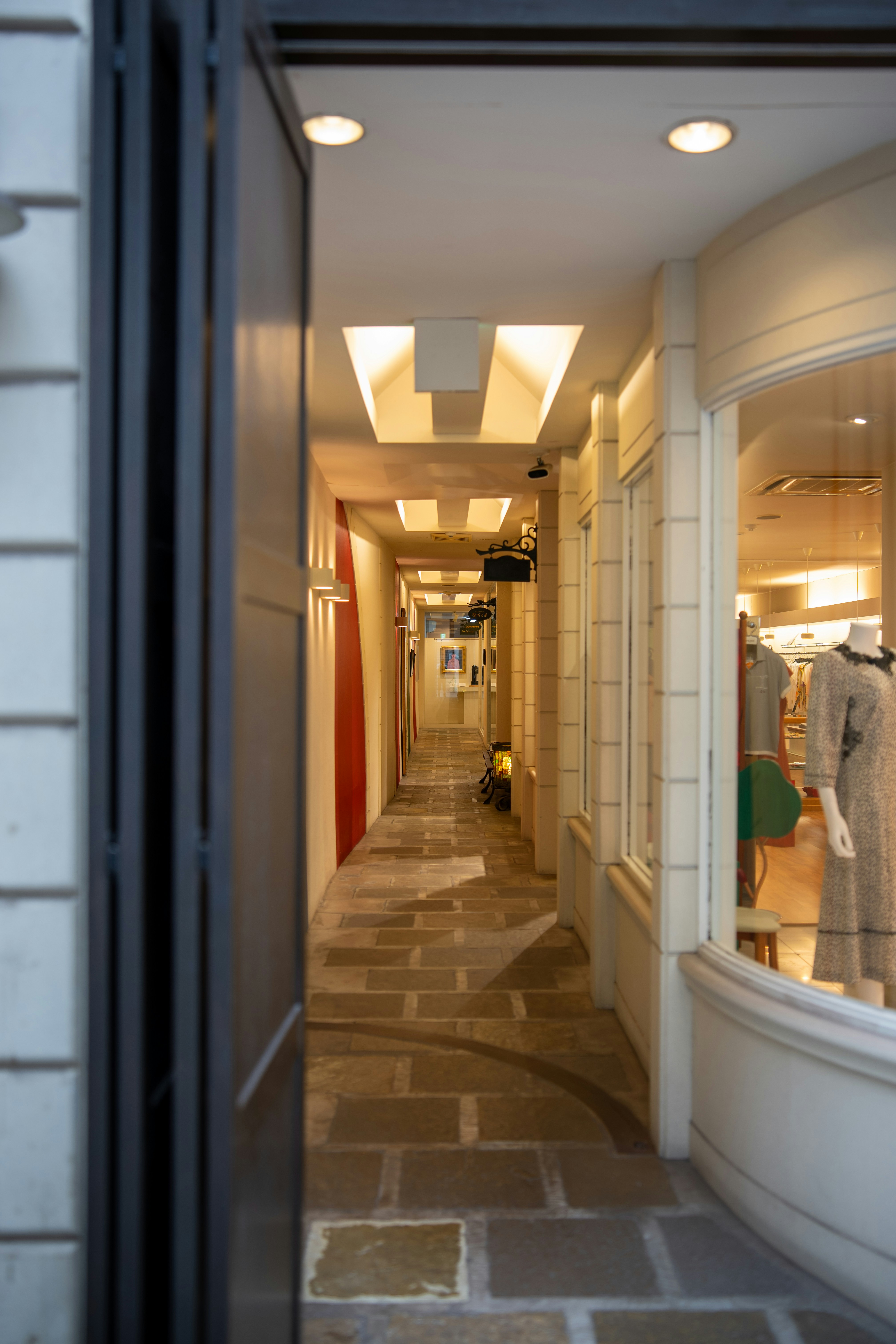A narrow stone walkway between shopfronts with warm recessed lighting in the ceiling