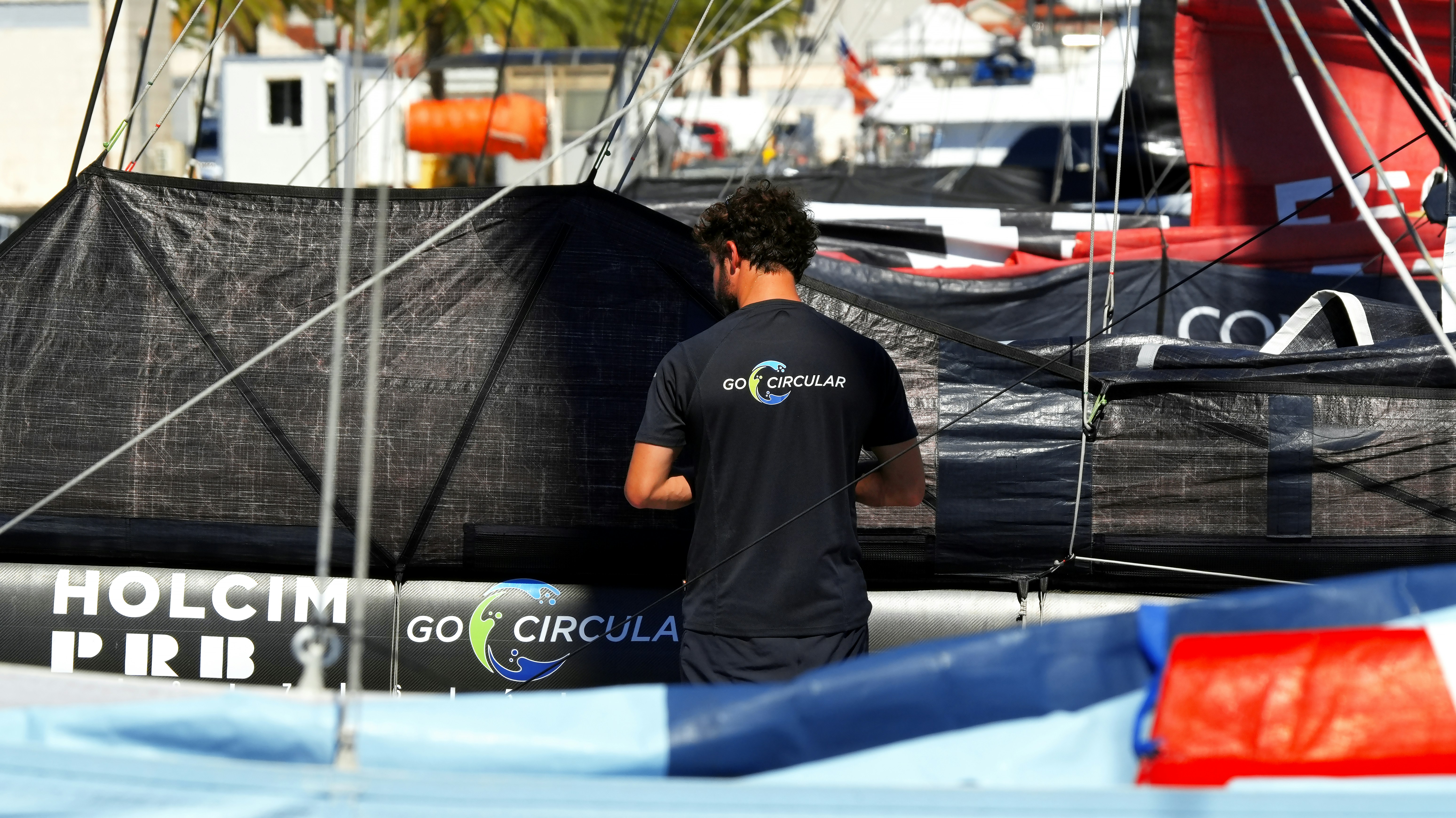 A person in a black shirt standing by a sailboat with black sails