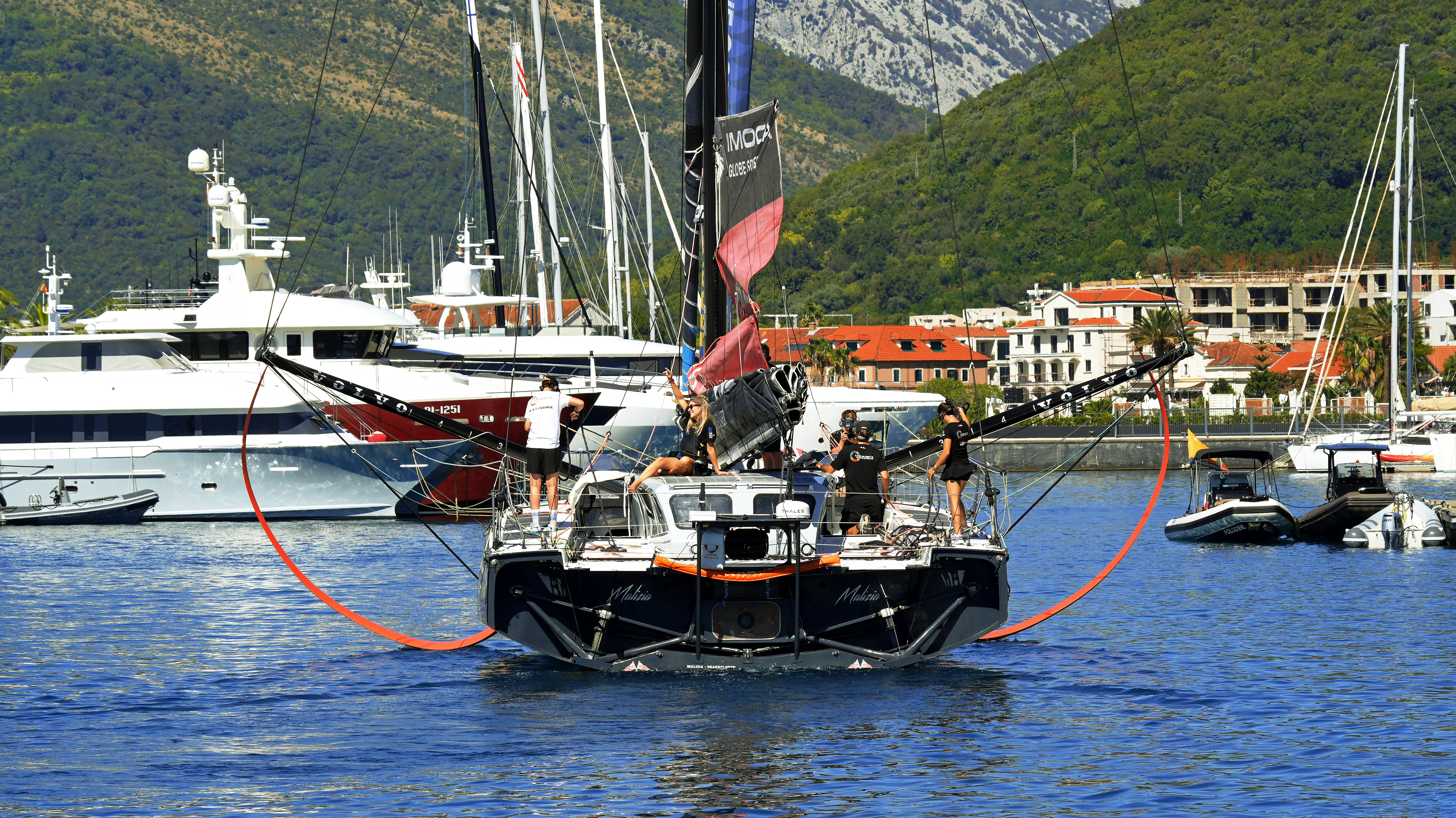 A racing sailboat with a crew on deck in a marina with yachts