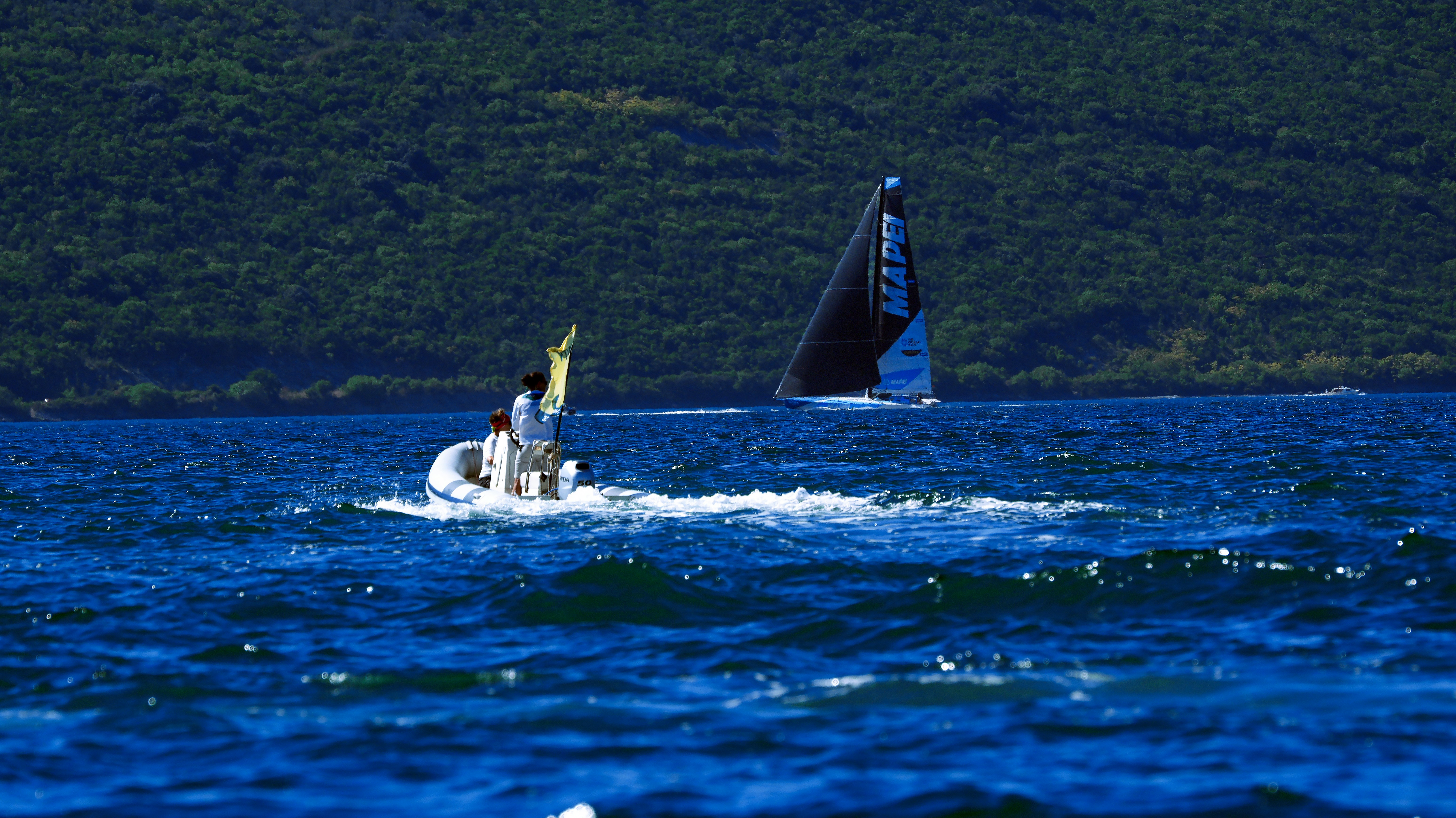 A small motorboat following a sailboat with a black sail on blue water