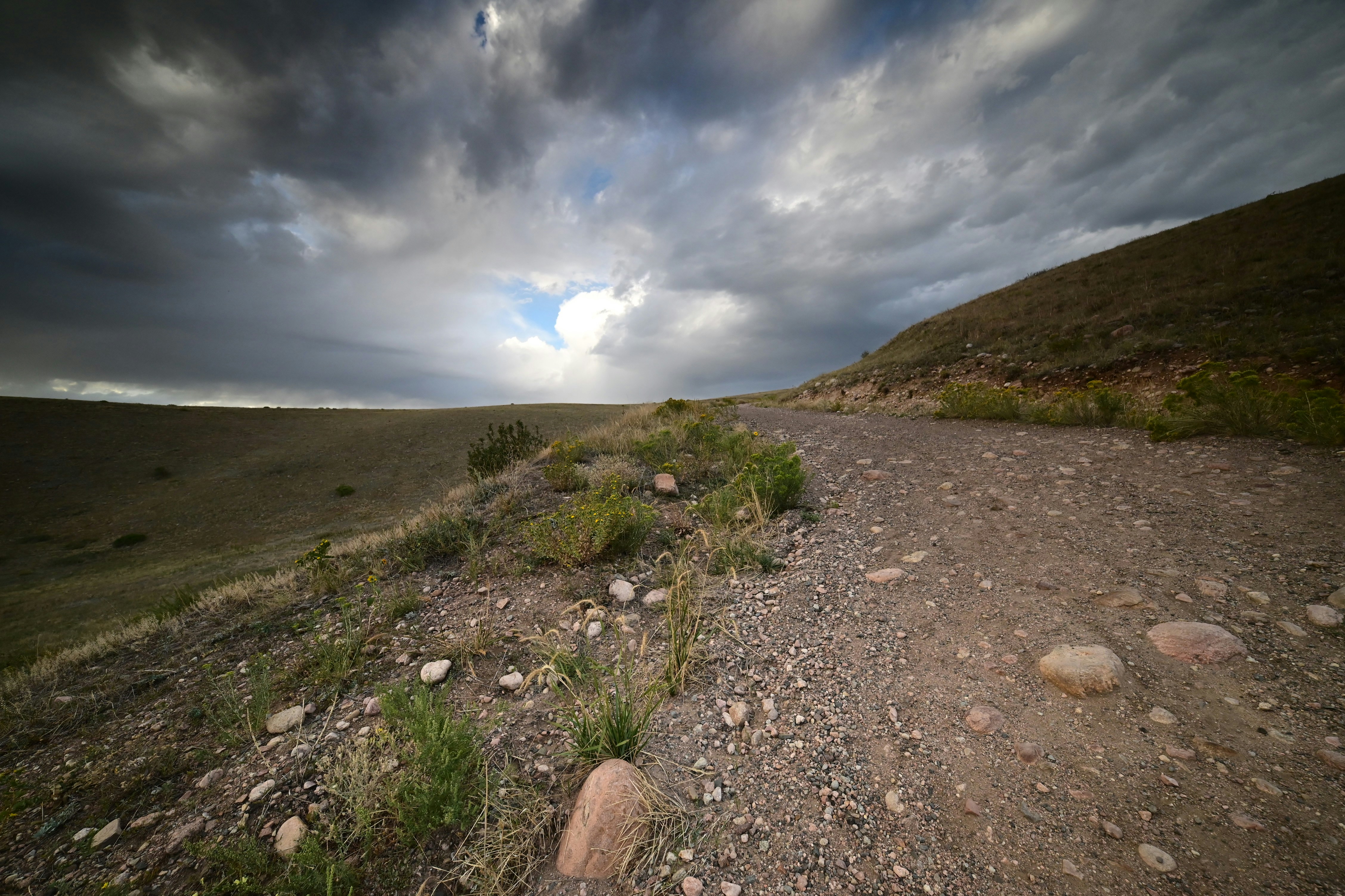 A gravel path winding through a grassy hillside under a dark cloudy sky