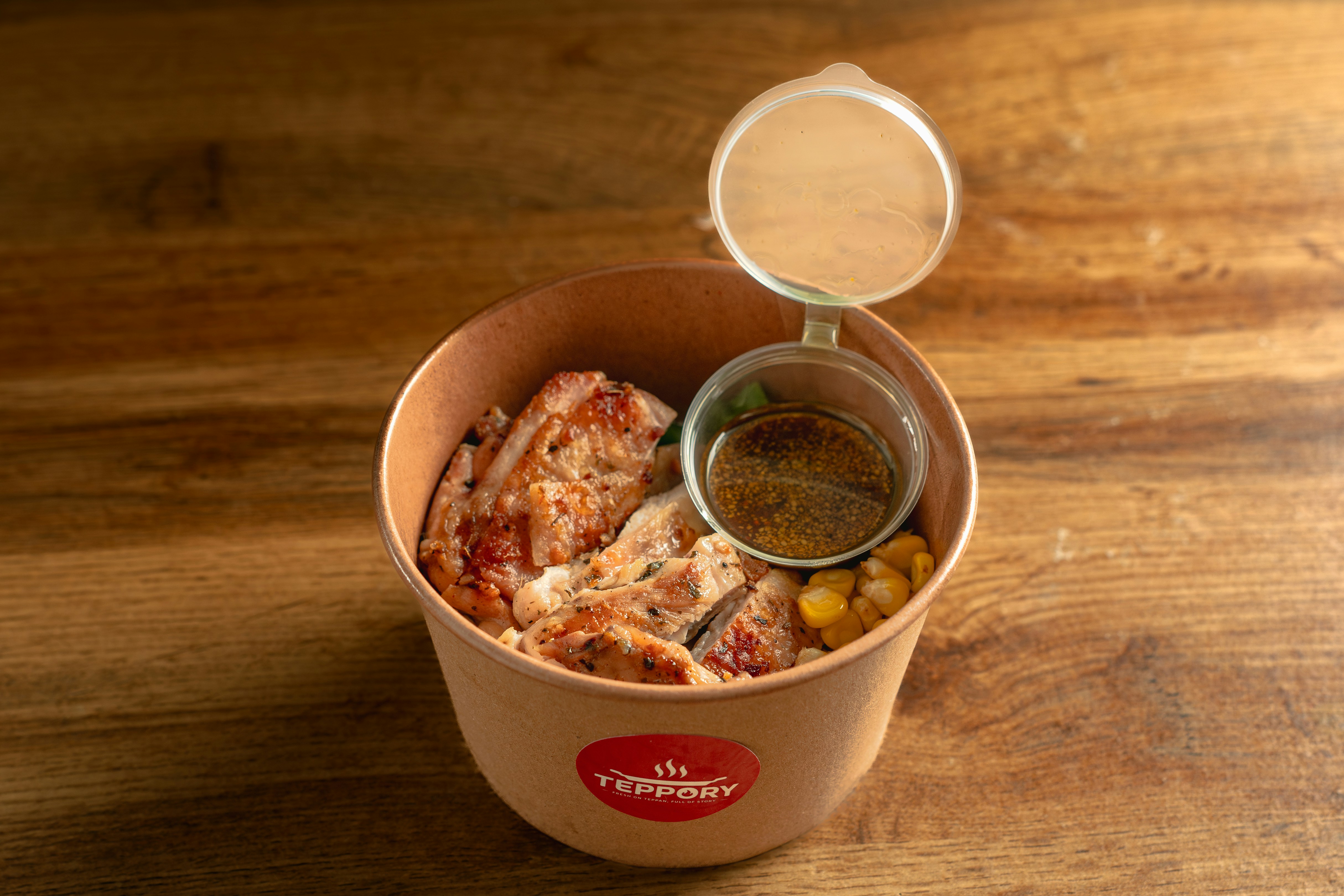 Gegrilltes Hähnchen mit Mais und Soße in einer Papierschüssel auf einem Holztisch