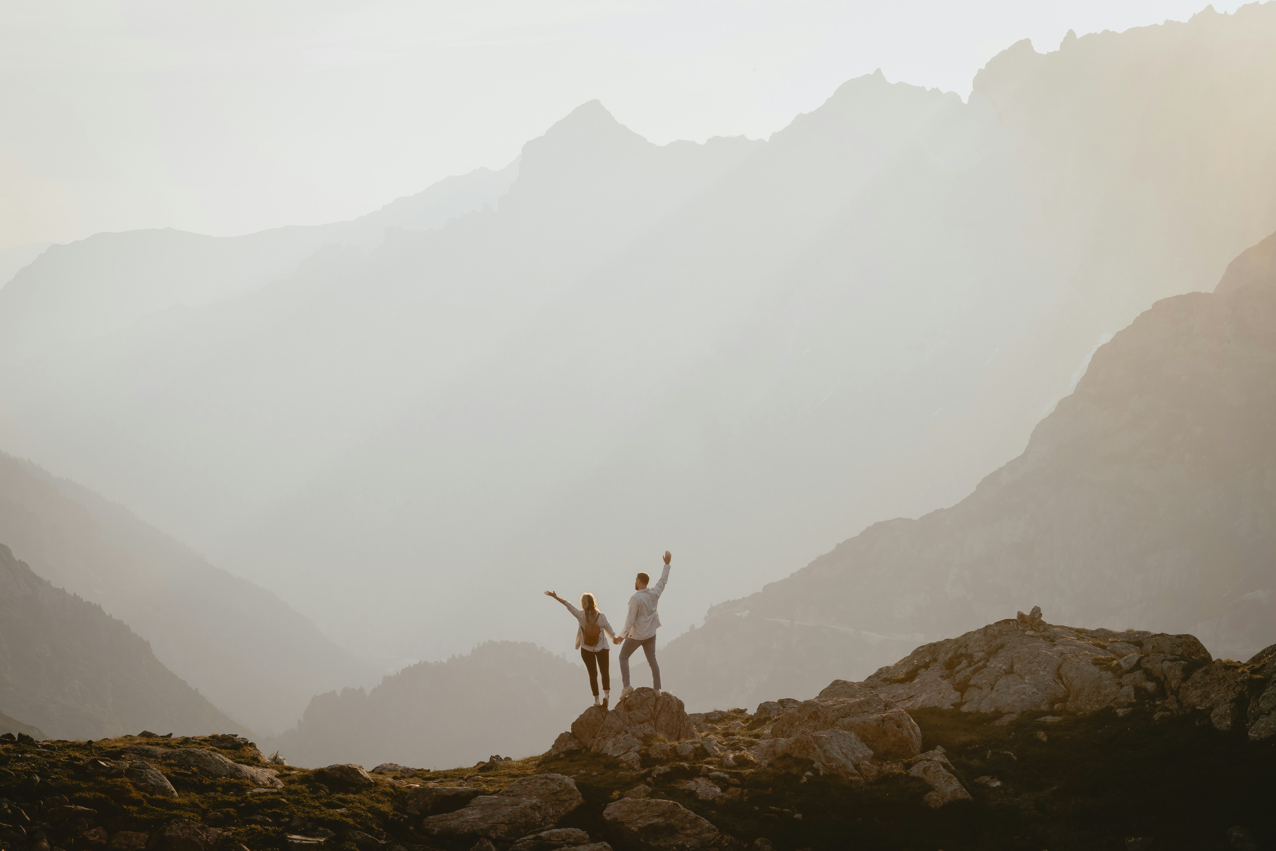 Two people holding hands on a rocky mountain peak in soft golden light