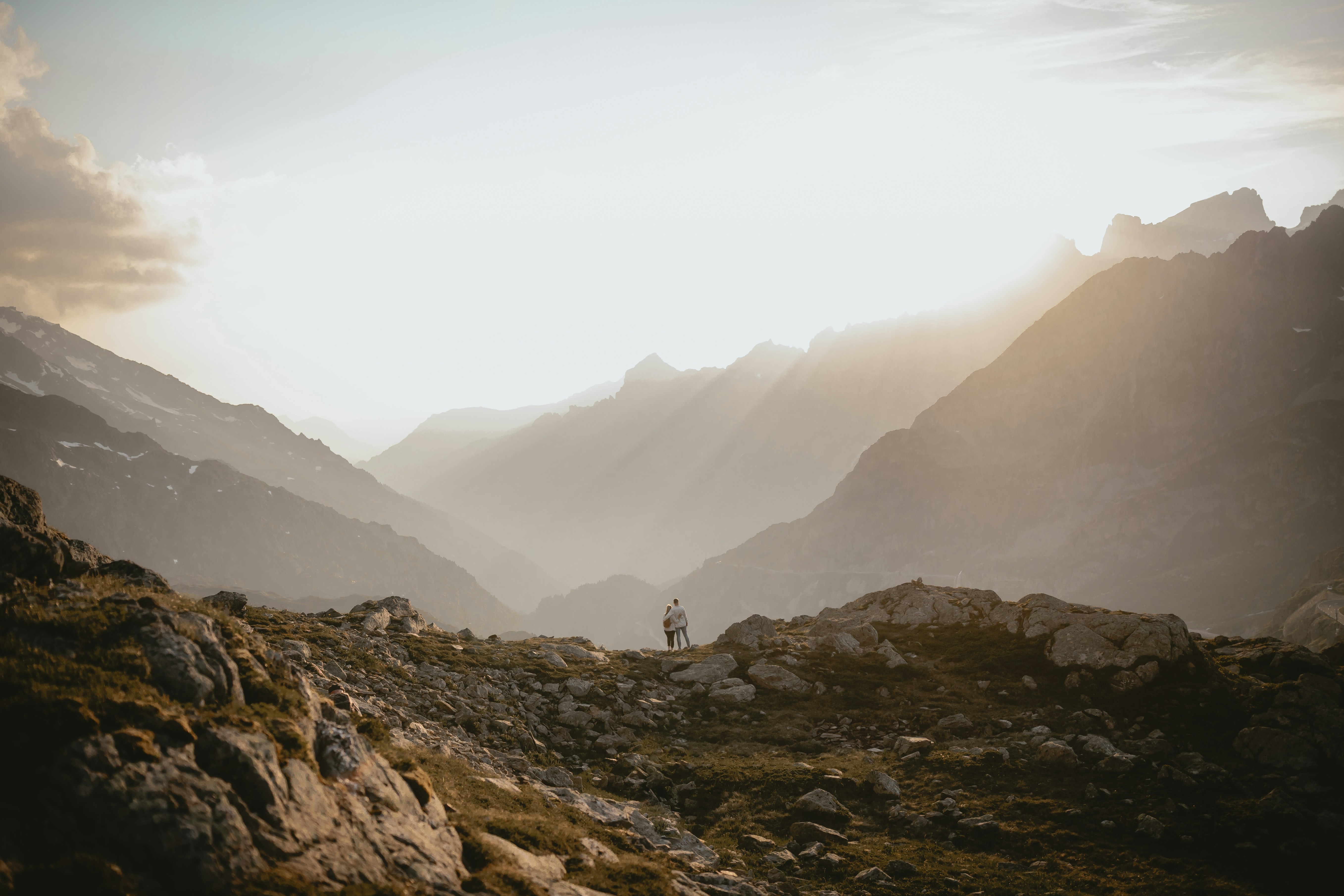 Two people on a rocky mountain ridge under a bright hazy sky
