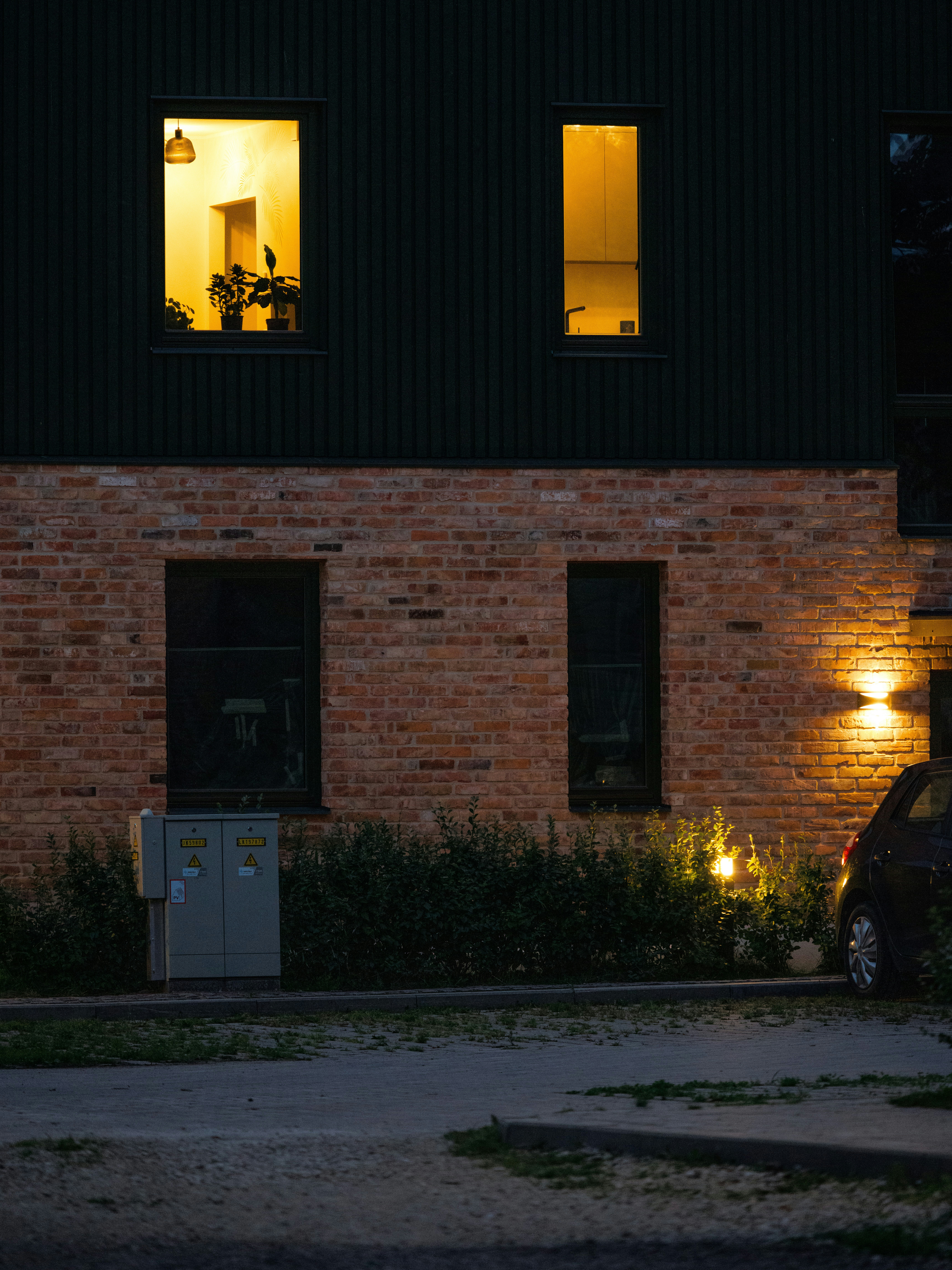 A brick building with glowing windows at night and a car parked outside