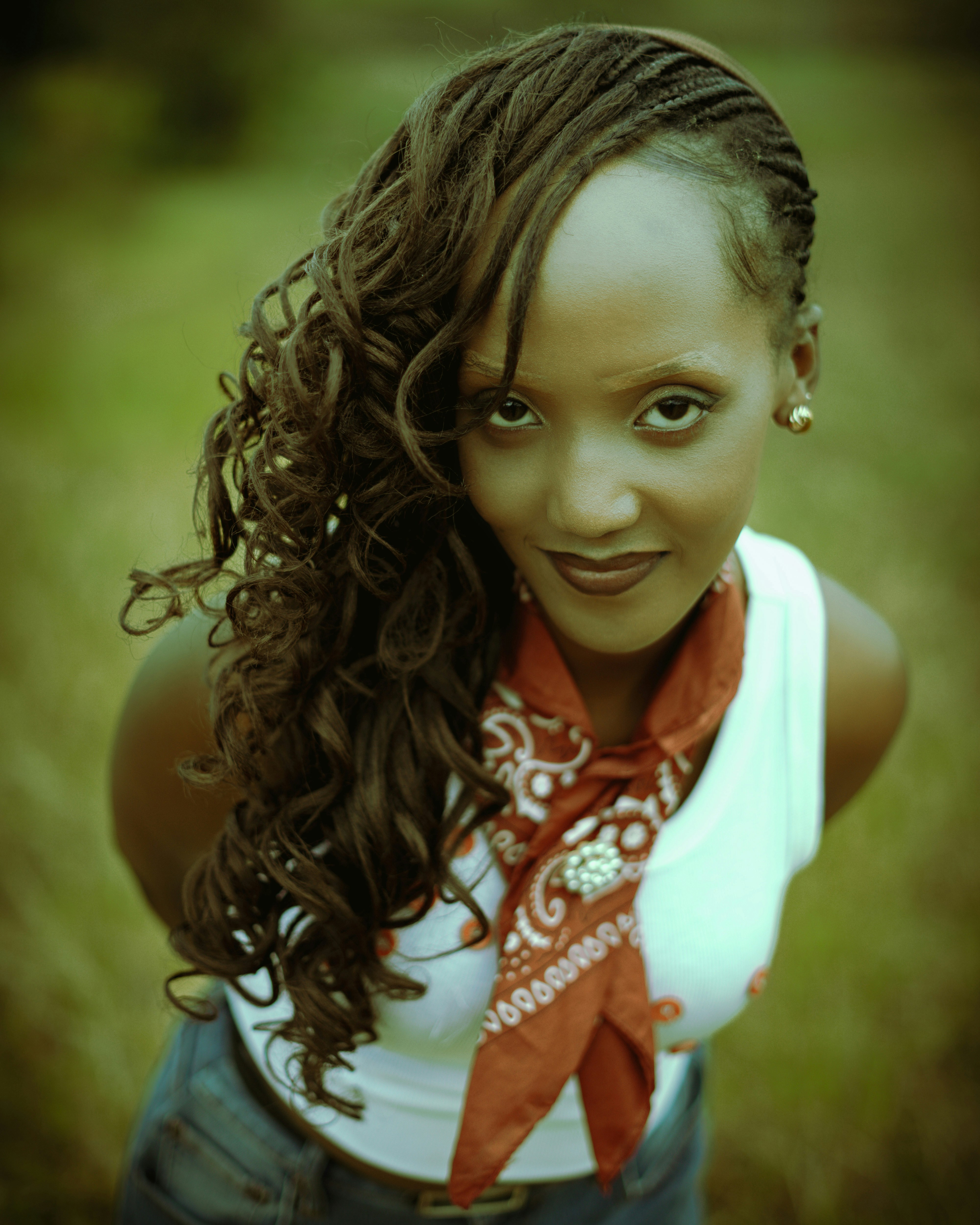 A woman with long curly hair wearing a white tank top and red bandana