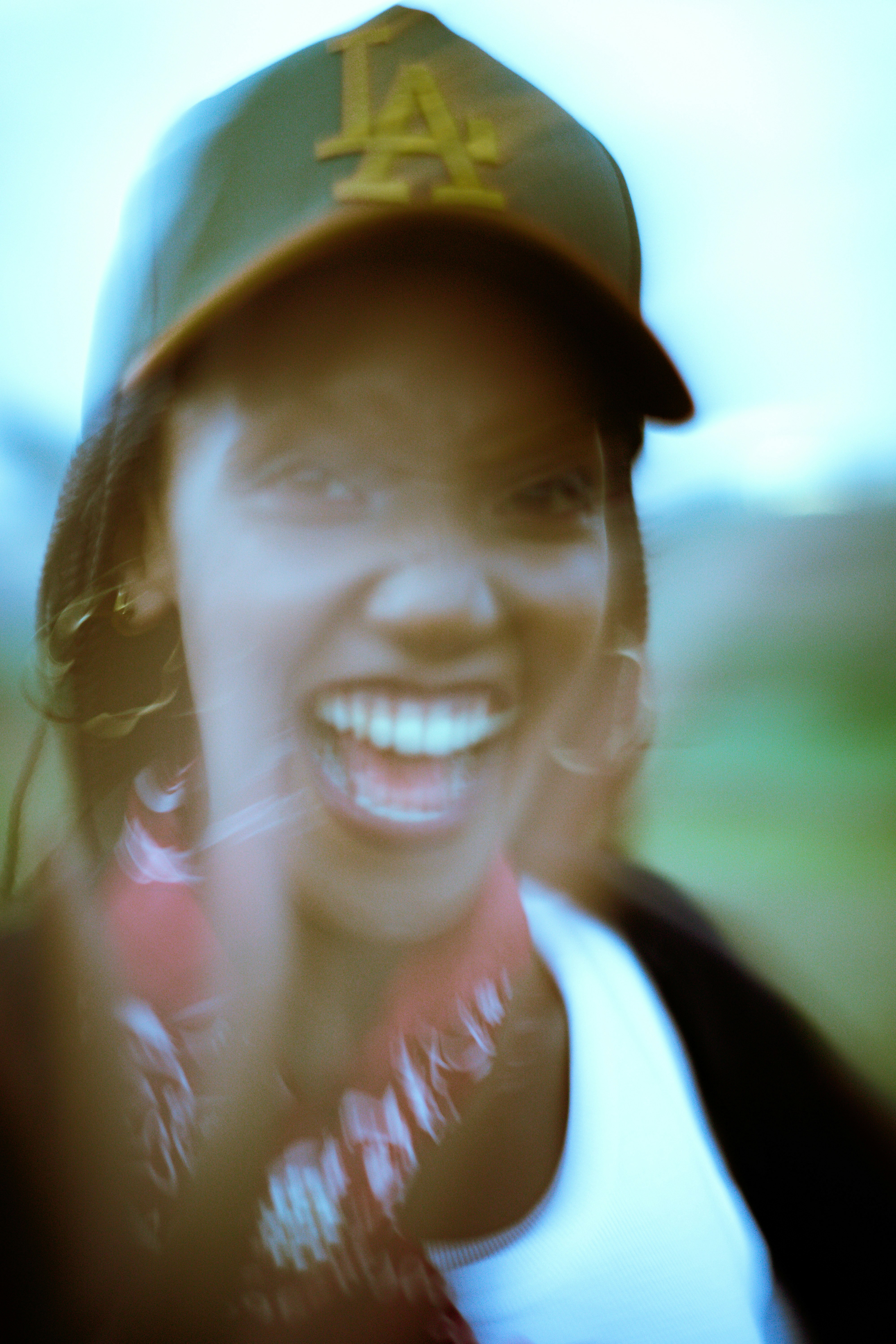 A person wearing a baseball cap and a red bandana laughing outdoors