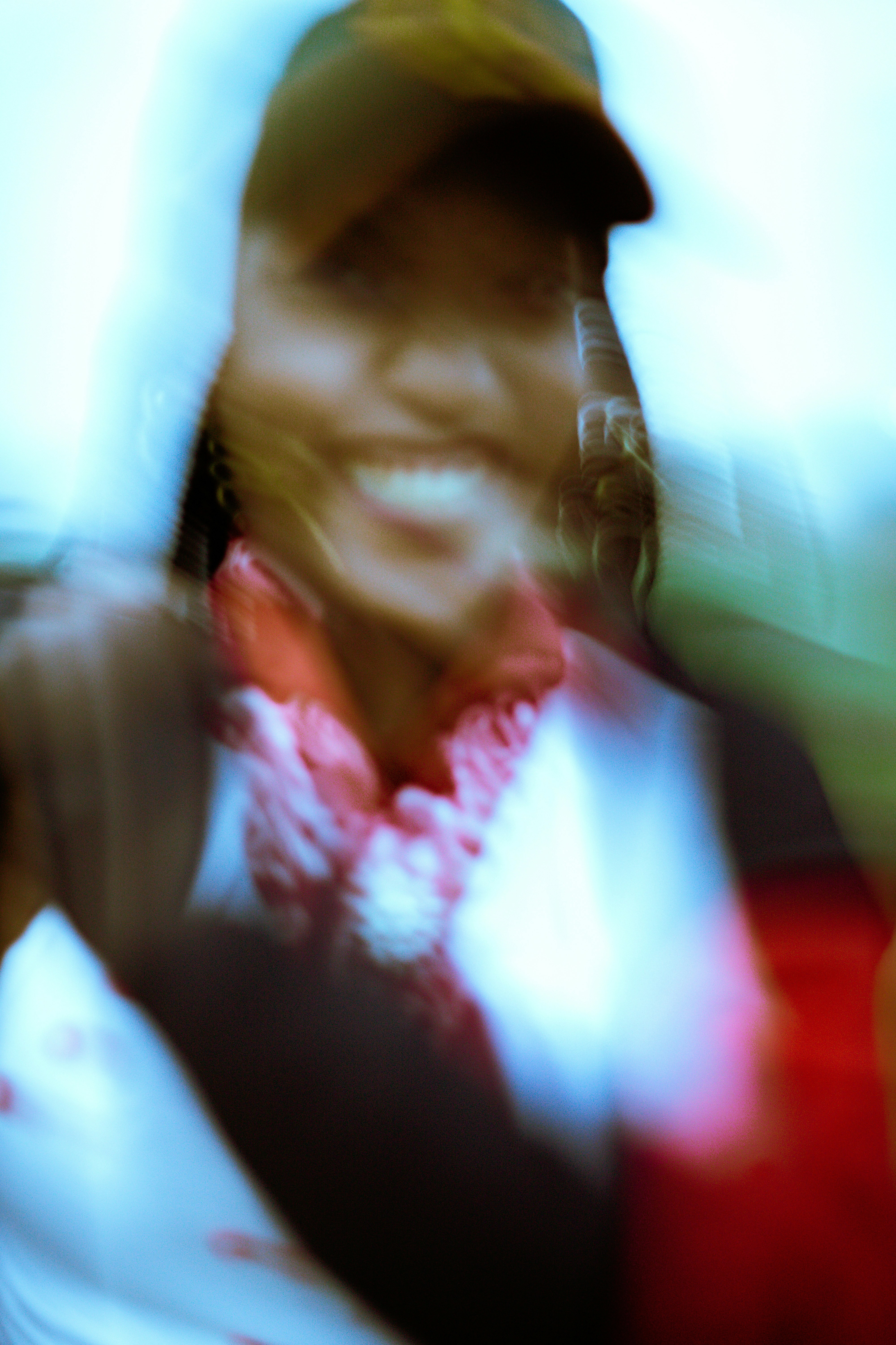 A person wearing a baseball cap and a red patterned scarf, motion blurred