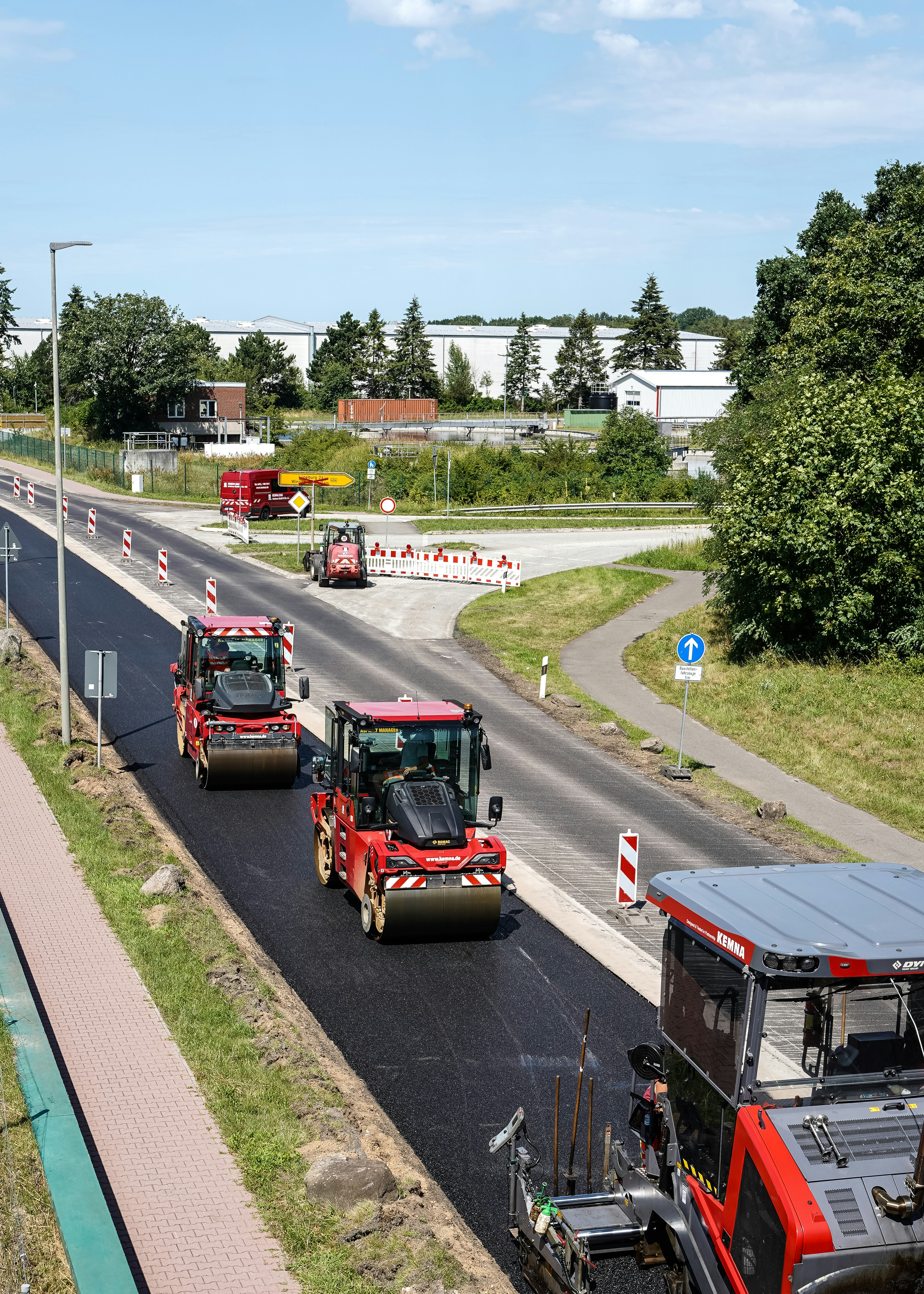 Three red road rollers compacting fresh asphalt on a sunny road construction site