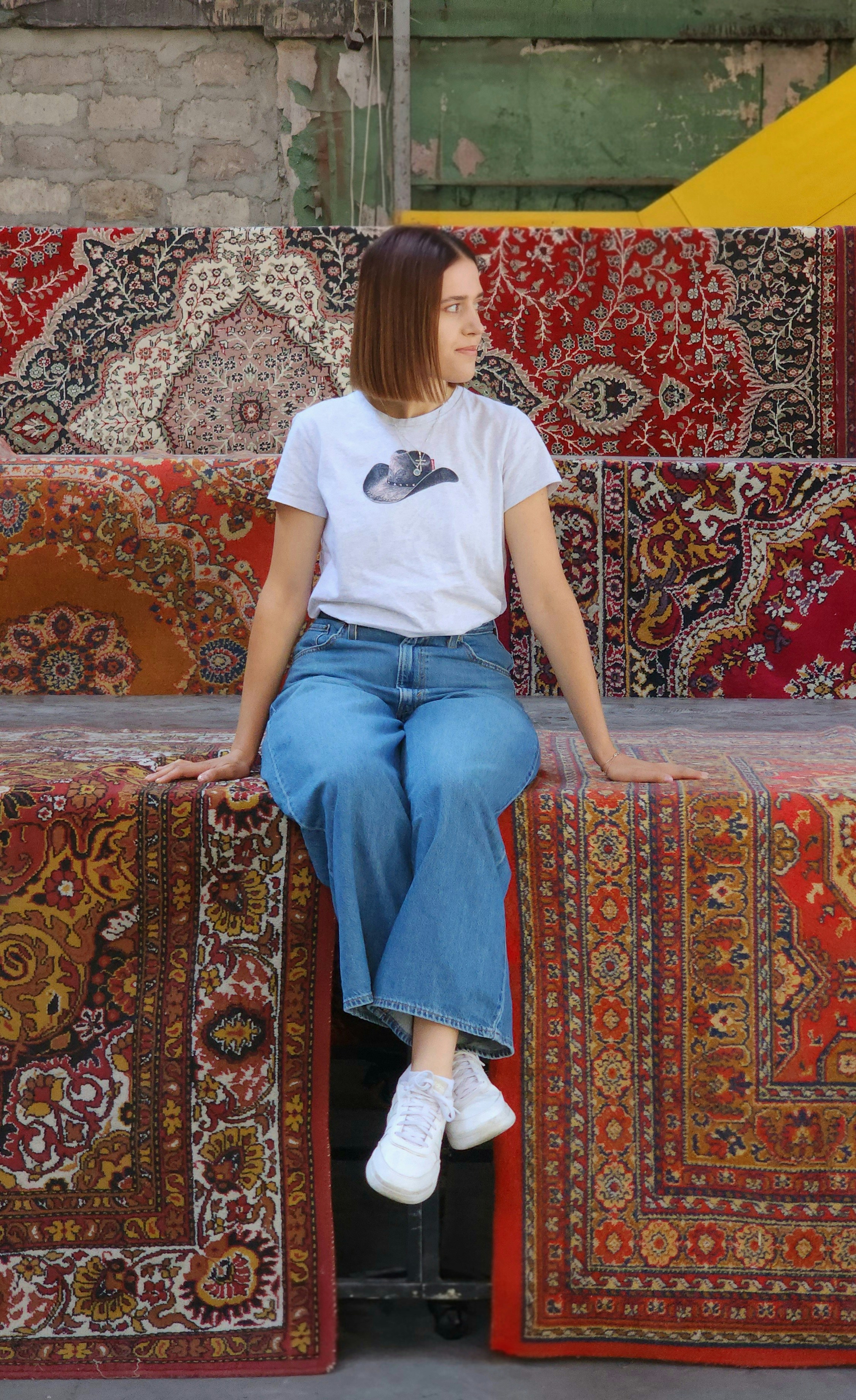 A woman in a white t-shirt and blue jeans sitting on patterned rugs