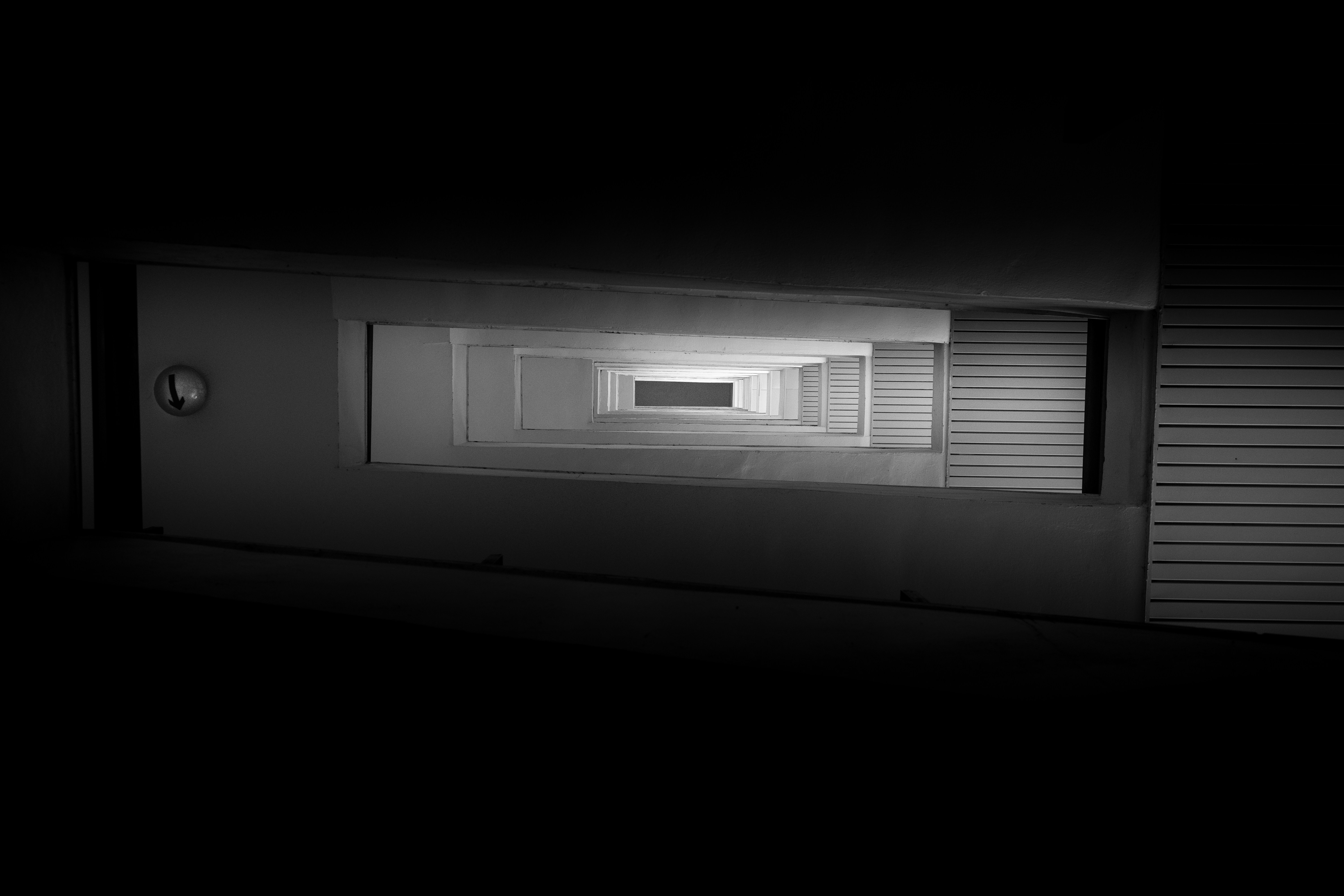 A receding view of rectangular concrete balconies in a dark stairwell