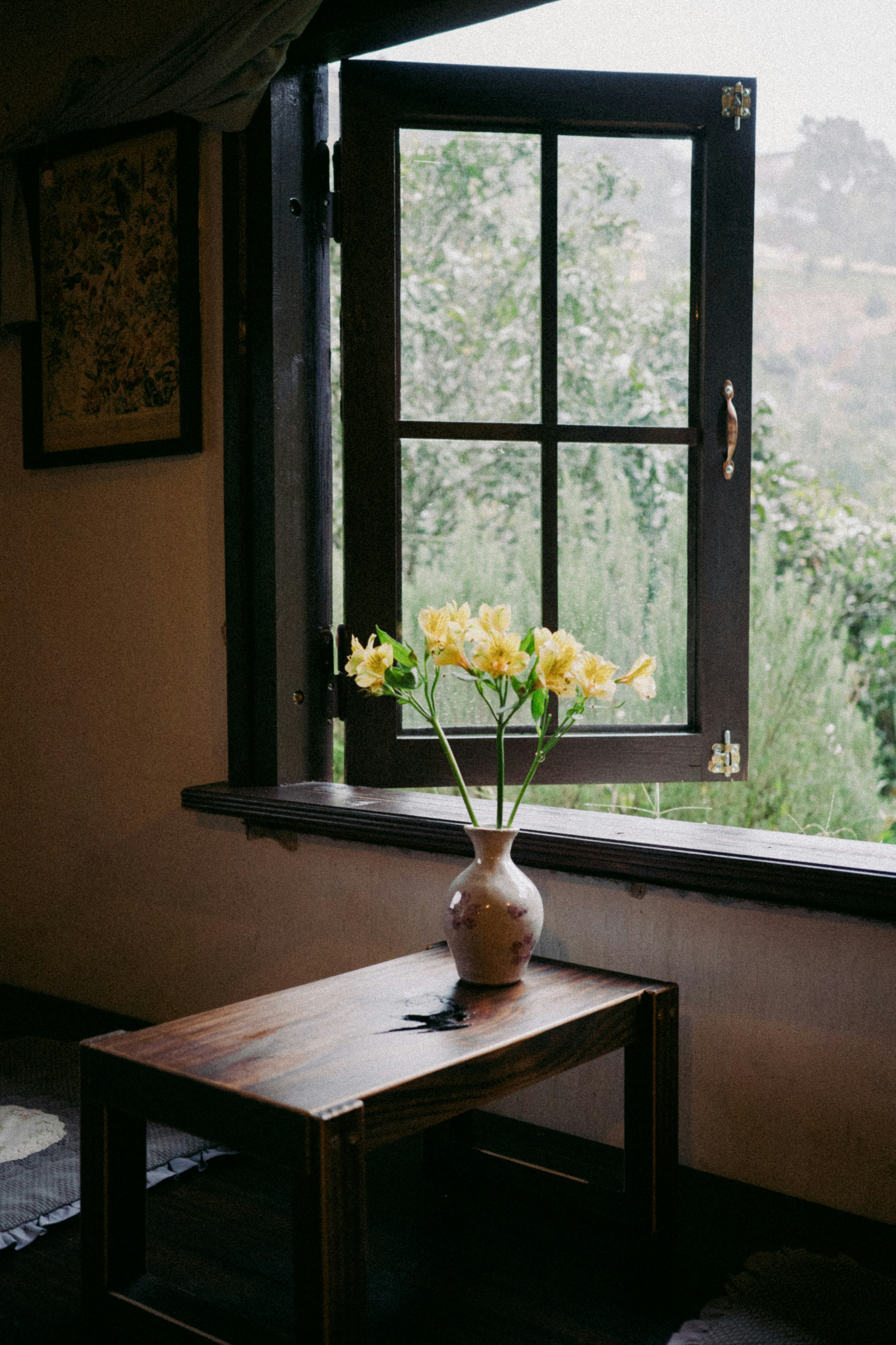Flores amarillas de alstroemeria en un jarrón de cerámica sobre una mesa de madera junto a una ventana