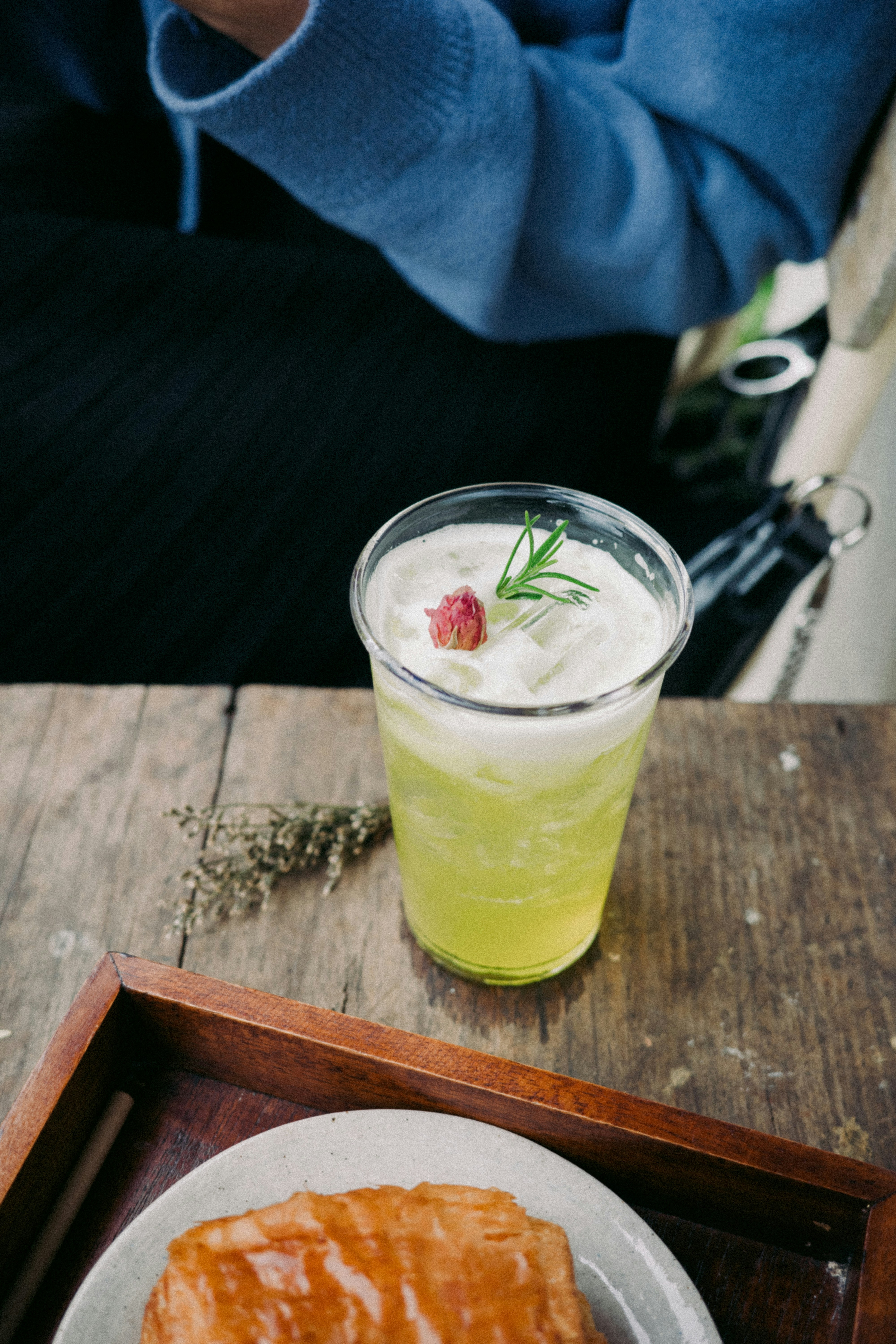 A green iced drink with a rosebud and rosemary on a wooden table