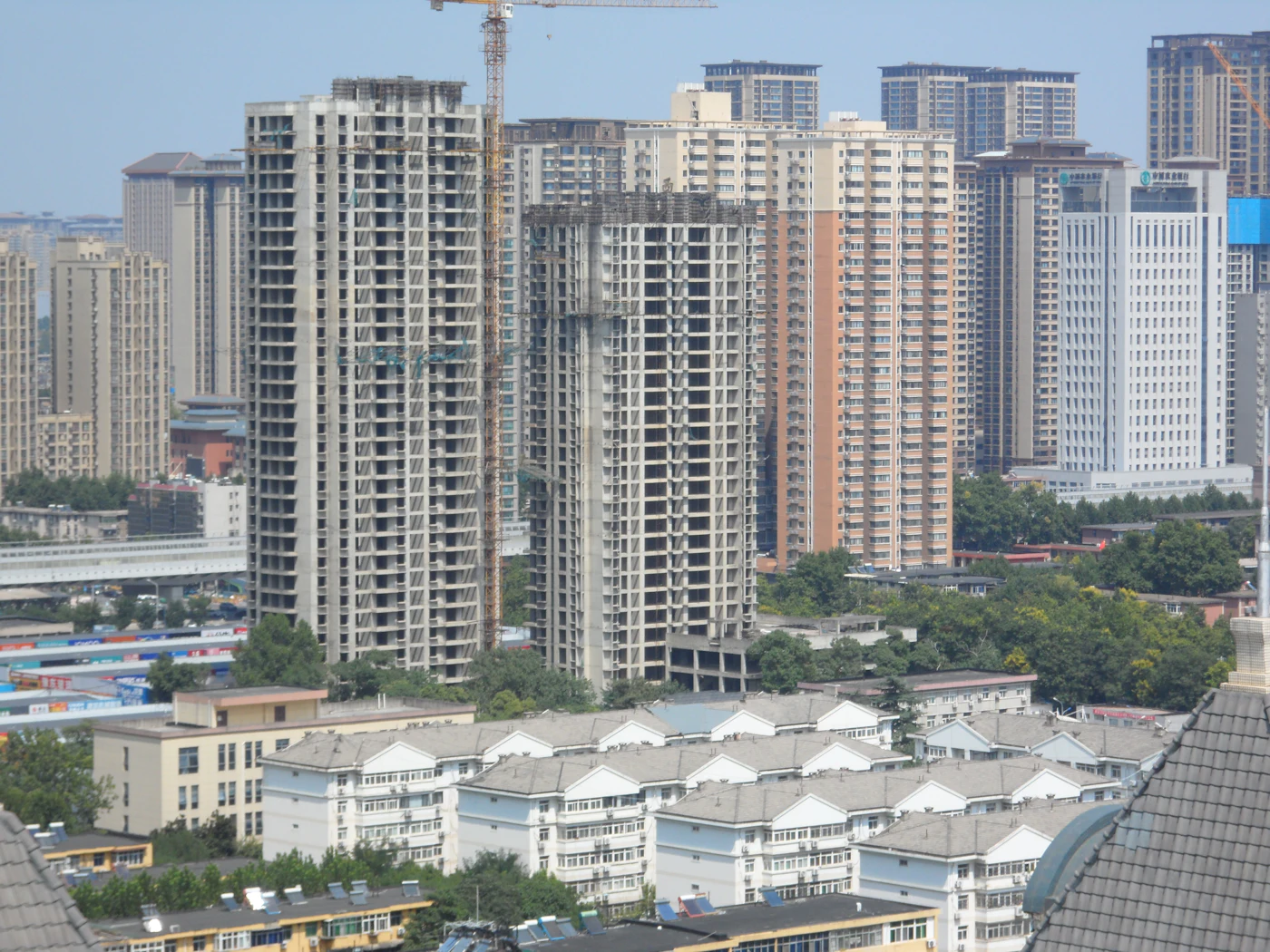 Two unfinished concrete high-rise towers under construction beside a crane in a dense city