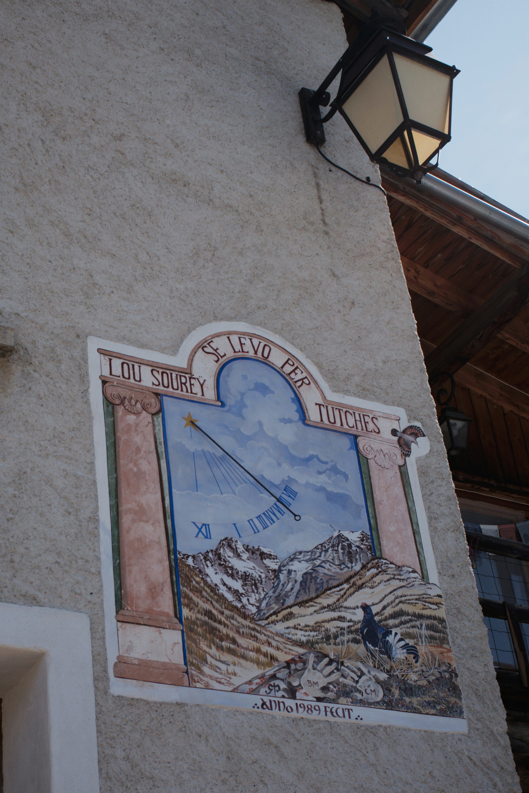 A painted sundial on a stucco wall with a black metal lantern above