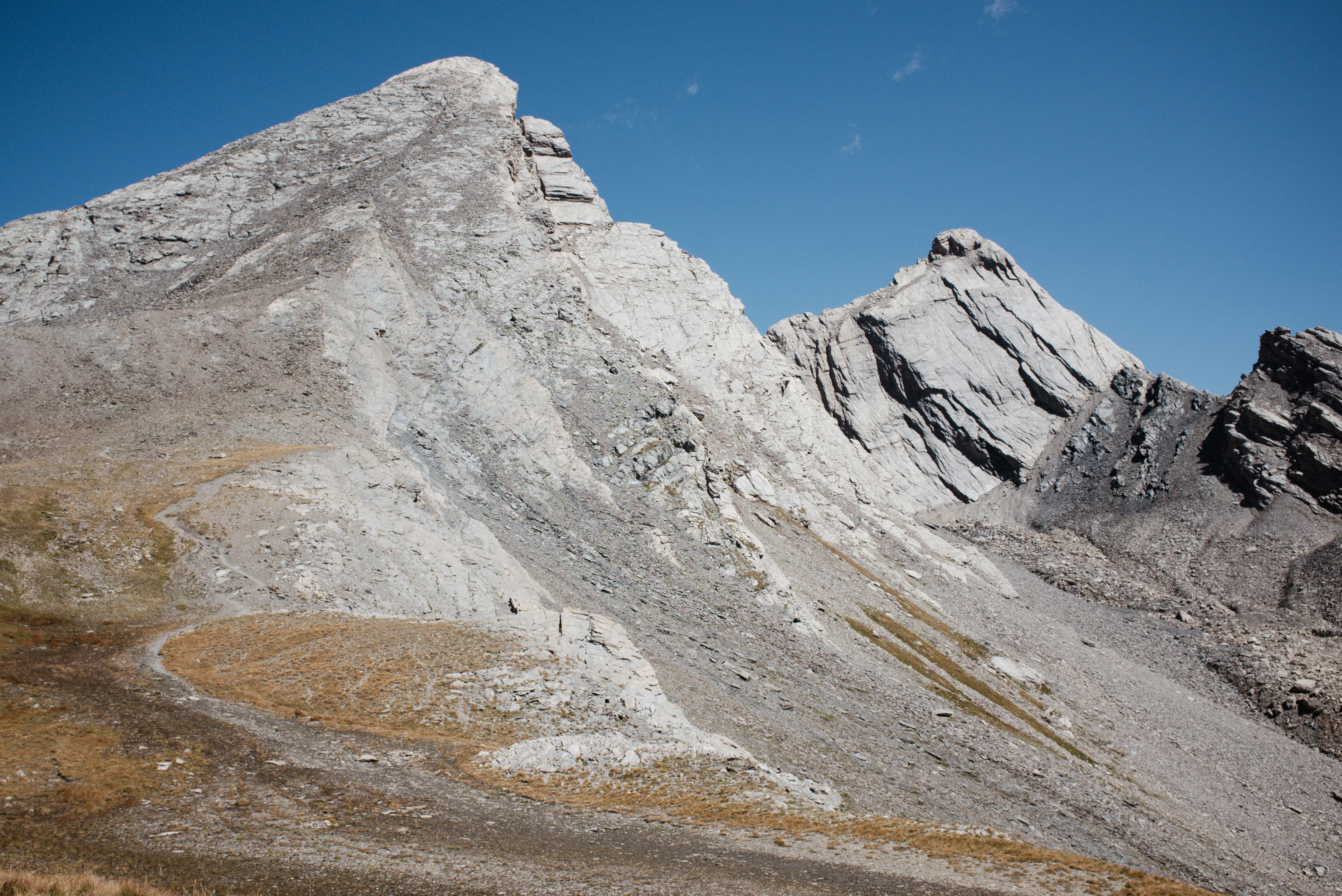 A winding dirt trail on a rocky mountain slope under a clear blue sky