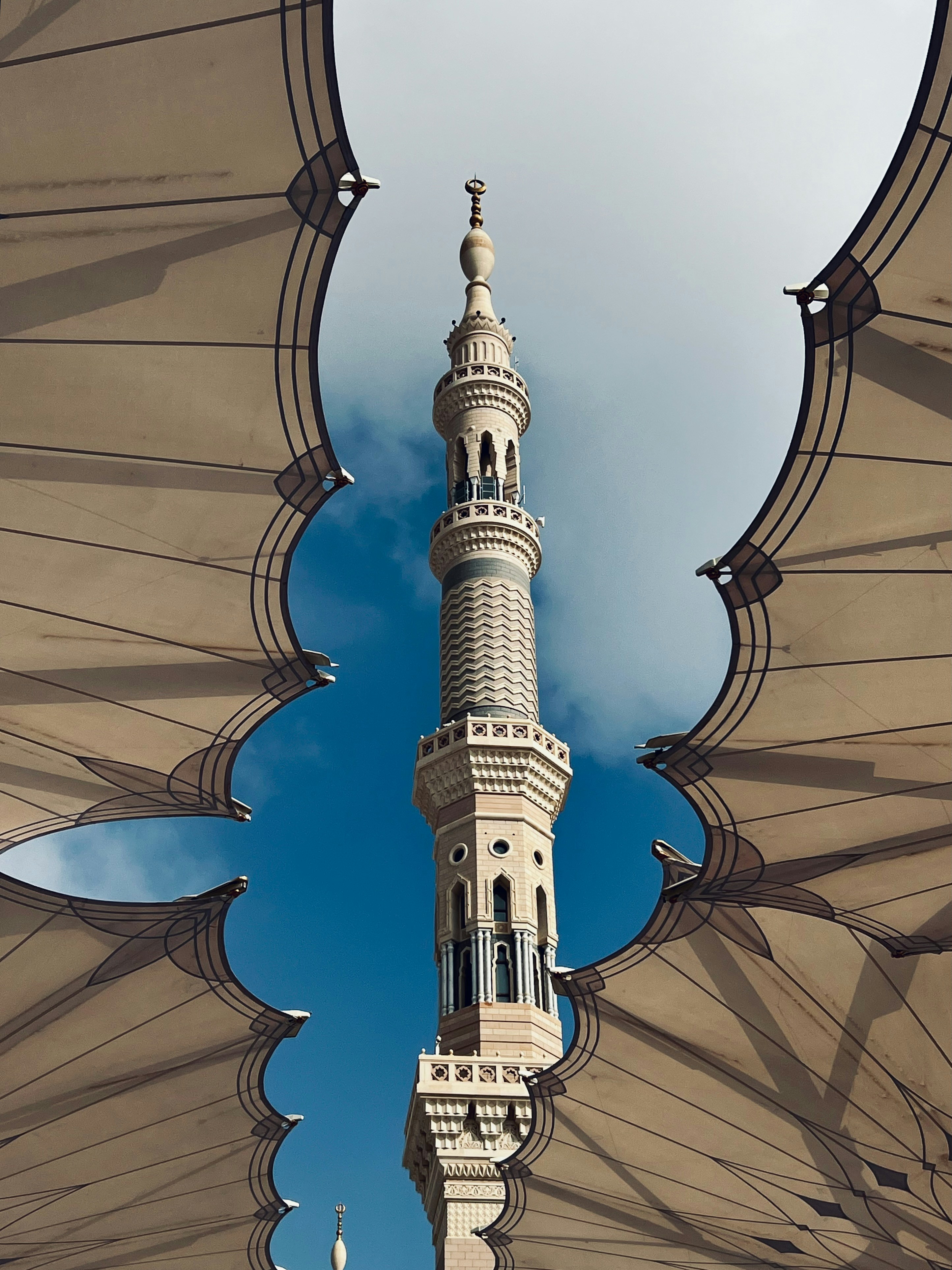 Um minarete alto emoldurado por grandes guarda-chuvas retráteis contra um céu azul