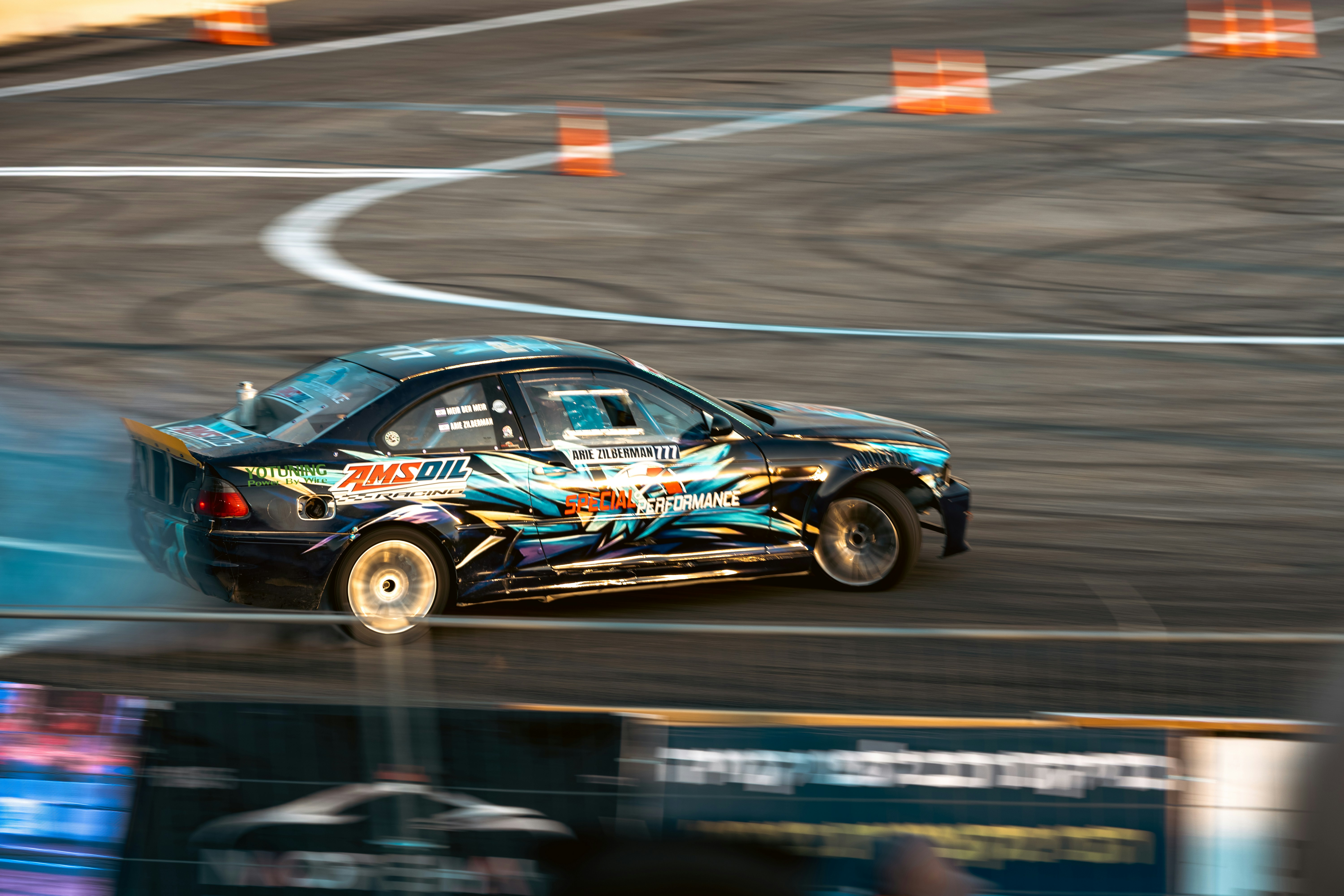 A black drift car with blue and yellow graphics sliding on an asphalt track