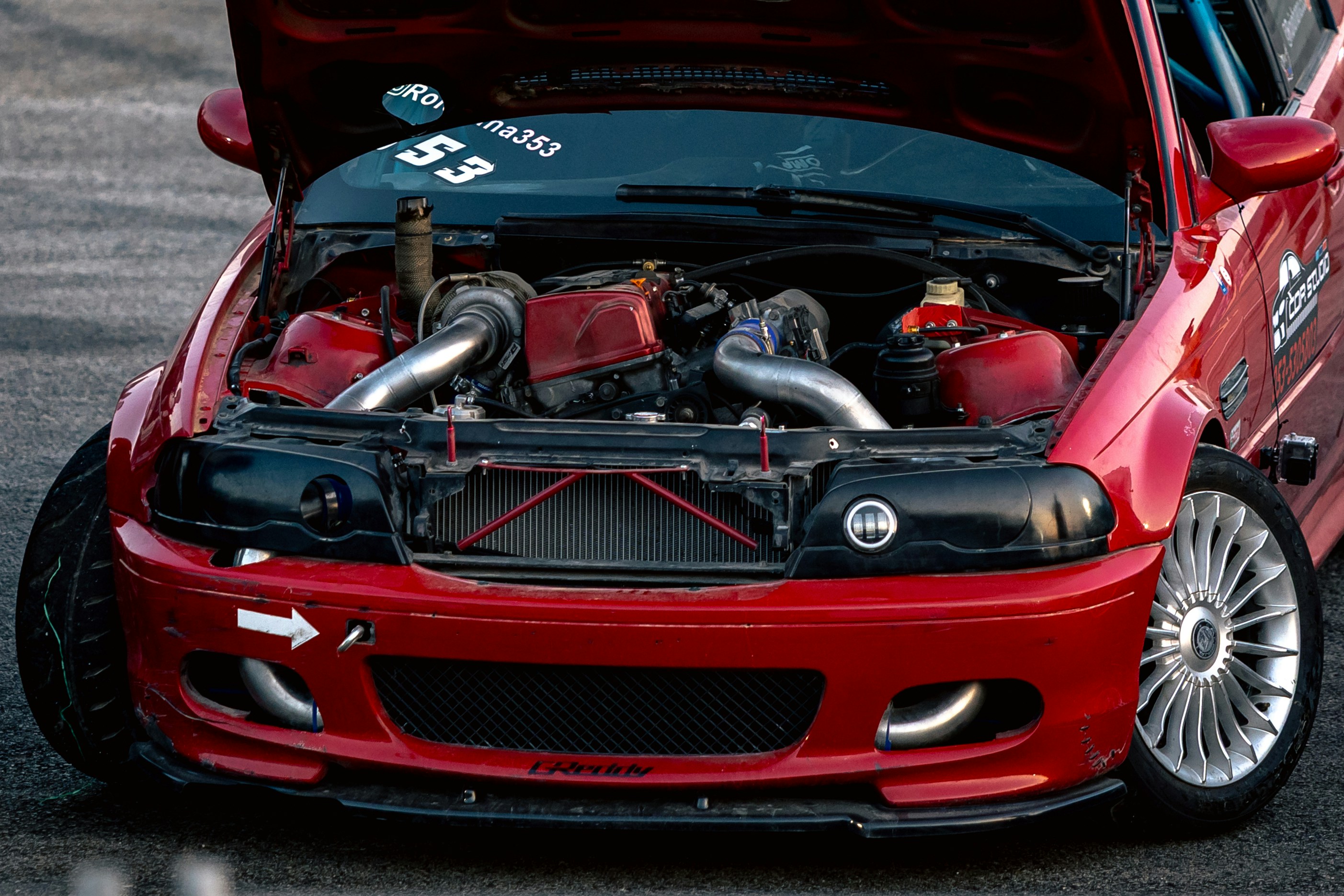 A red drift car with an open hood revealing a turbocharged engine
