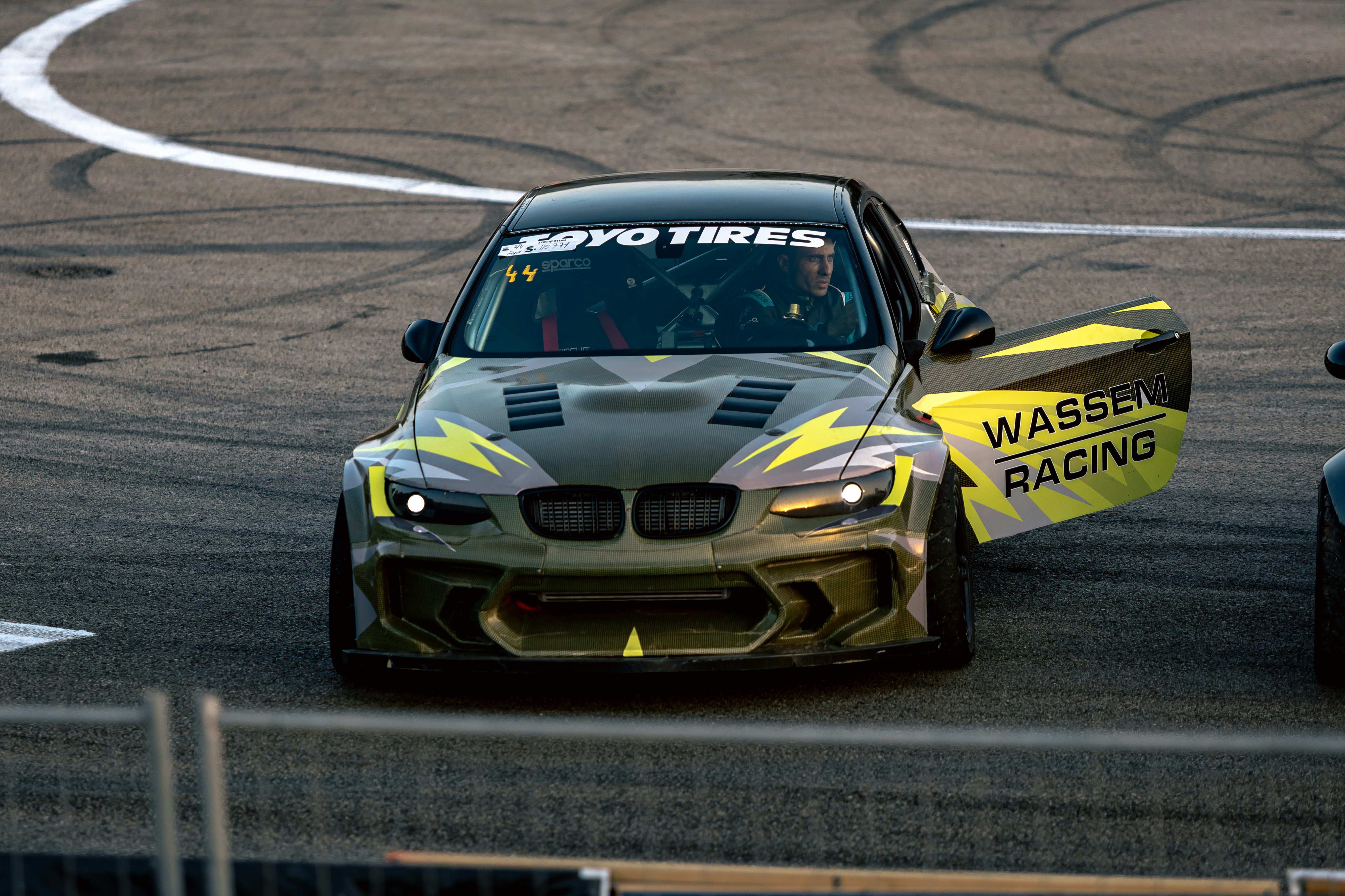 A modified BMW drift car with an open door on an asphalt track